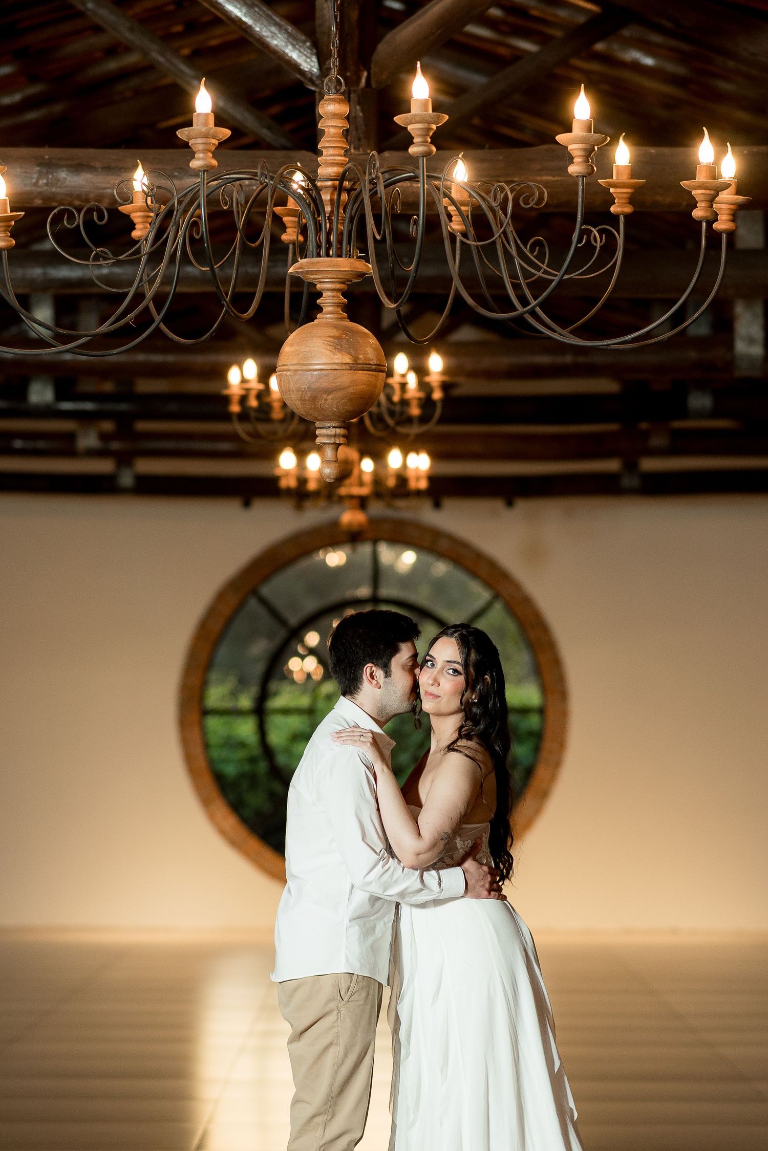 Couple sharing a romantic kiss under a rustic candlelit chandelier in an elegant barn wedding venue.