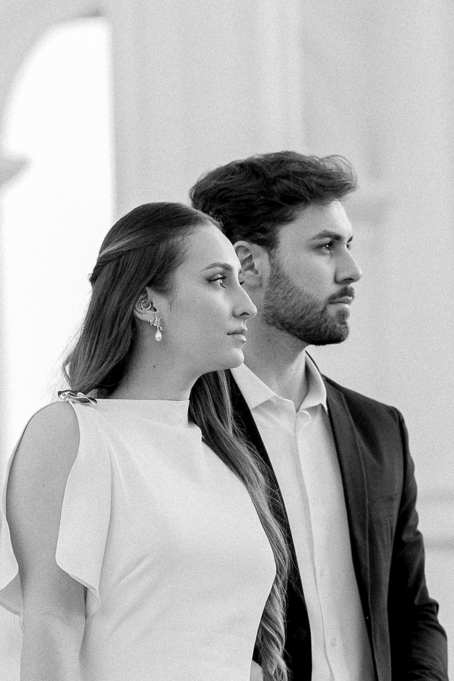 Black and white portrait of an elegant couple in formal attire gazing thoughtfully into the distance.