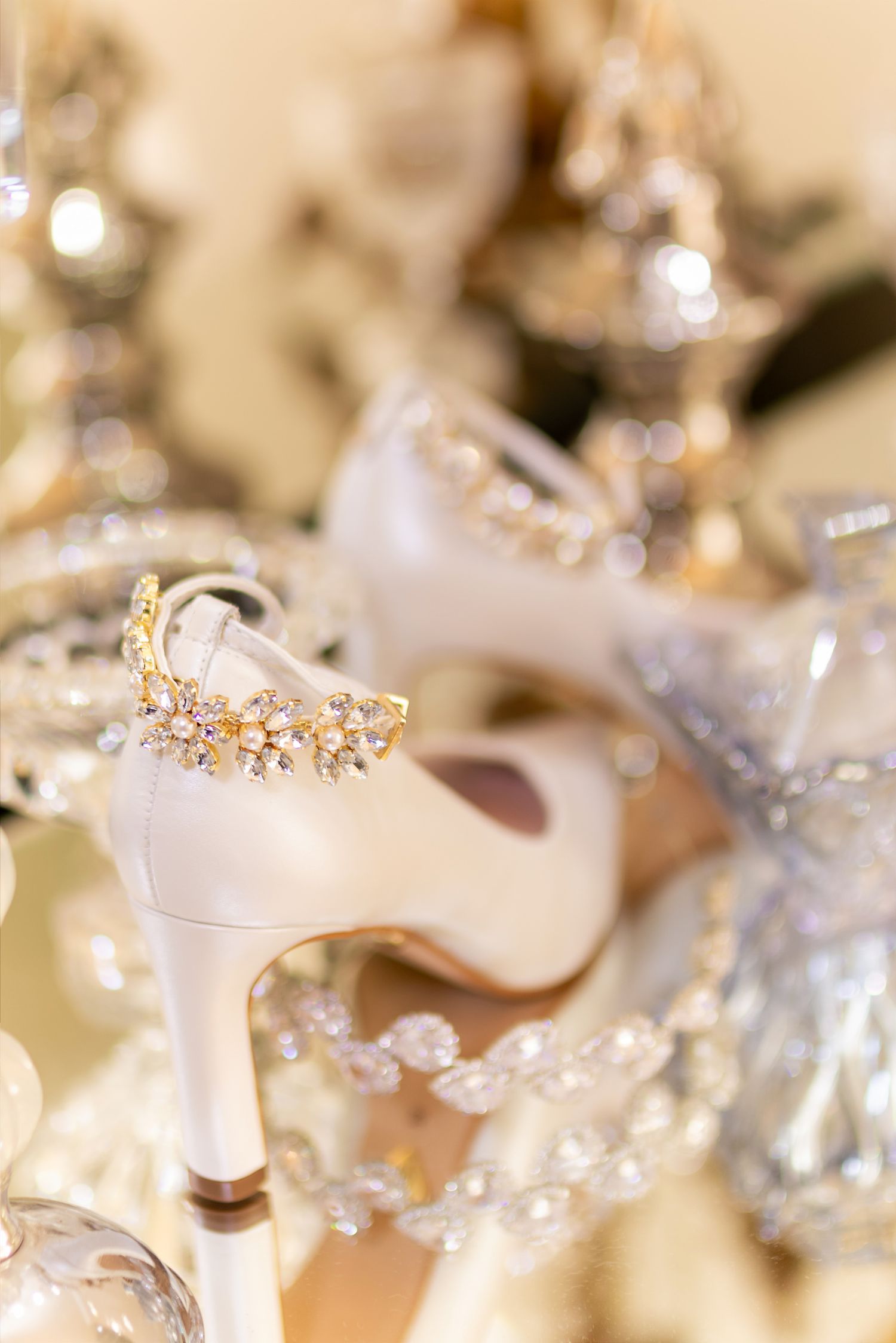 Elegant white bridal heels adorned with gold crystal jewelry on a glamorous gold mirrored surface.