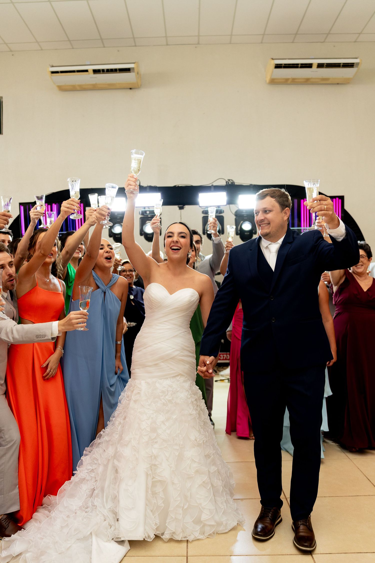 Bride and groom raise champagne glasses with guests celebrating at a wedding reception.