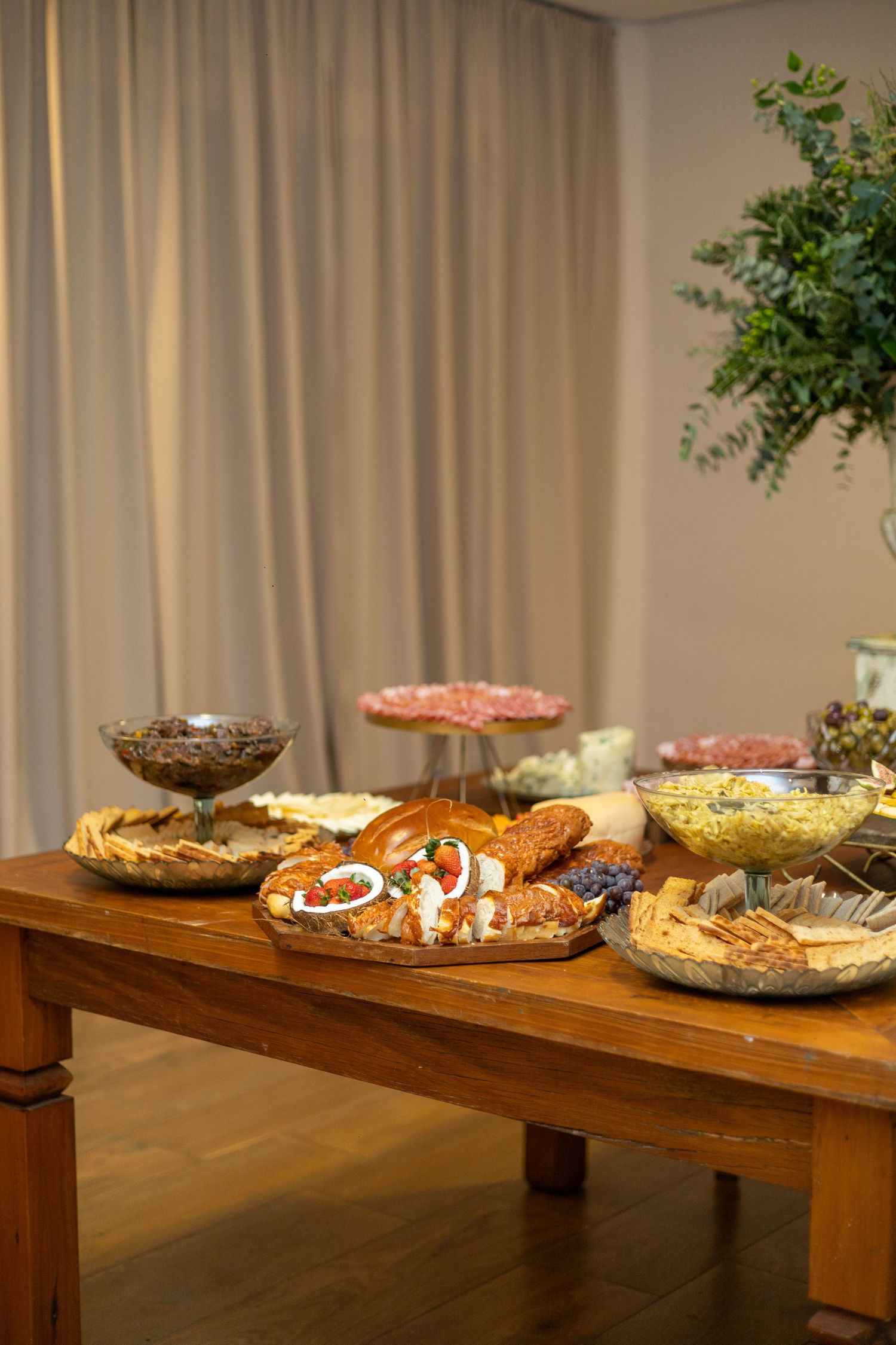 Elegant wooden buffet table with assorted appetizers, charcuterie, and snacks arranged on decorative platters at an event.