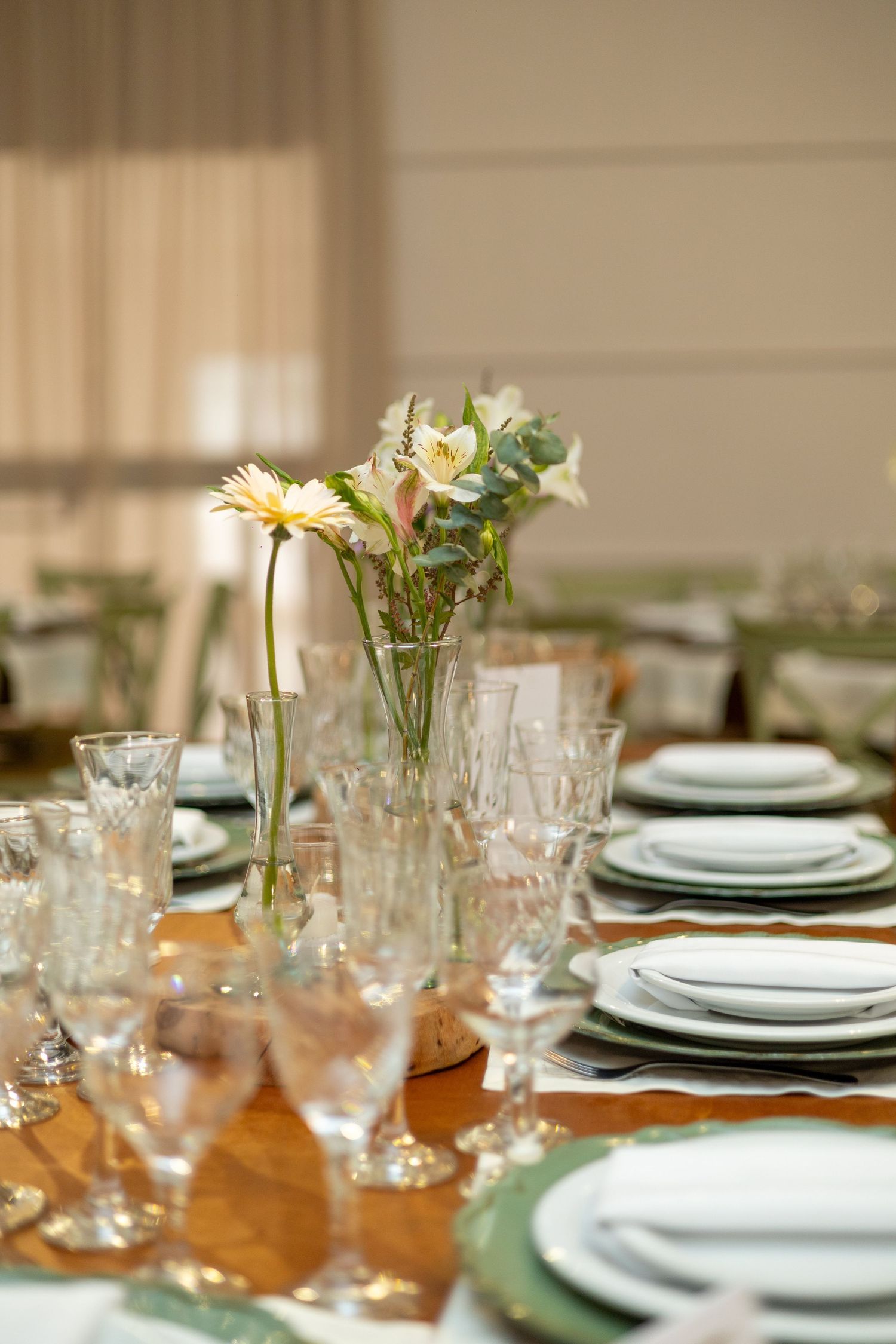Elegant wedding table setting with crystal glasses, white plates on green chargers, and floral centerpiece with yellow gerberas.