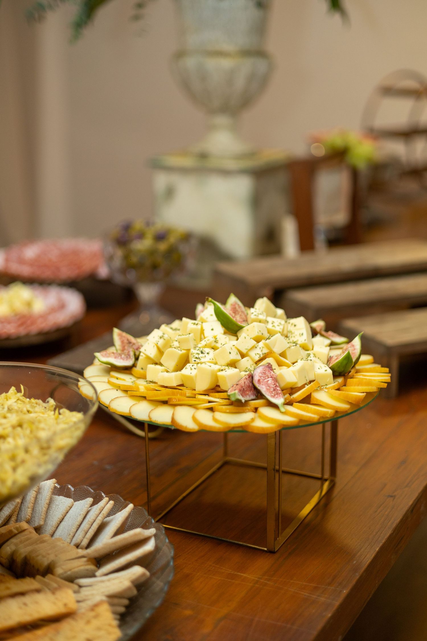 Elegant cheese and fruit platter with figs on a gold stand at a catered event buffet table.