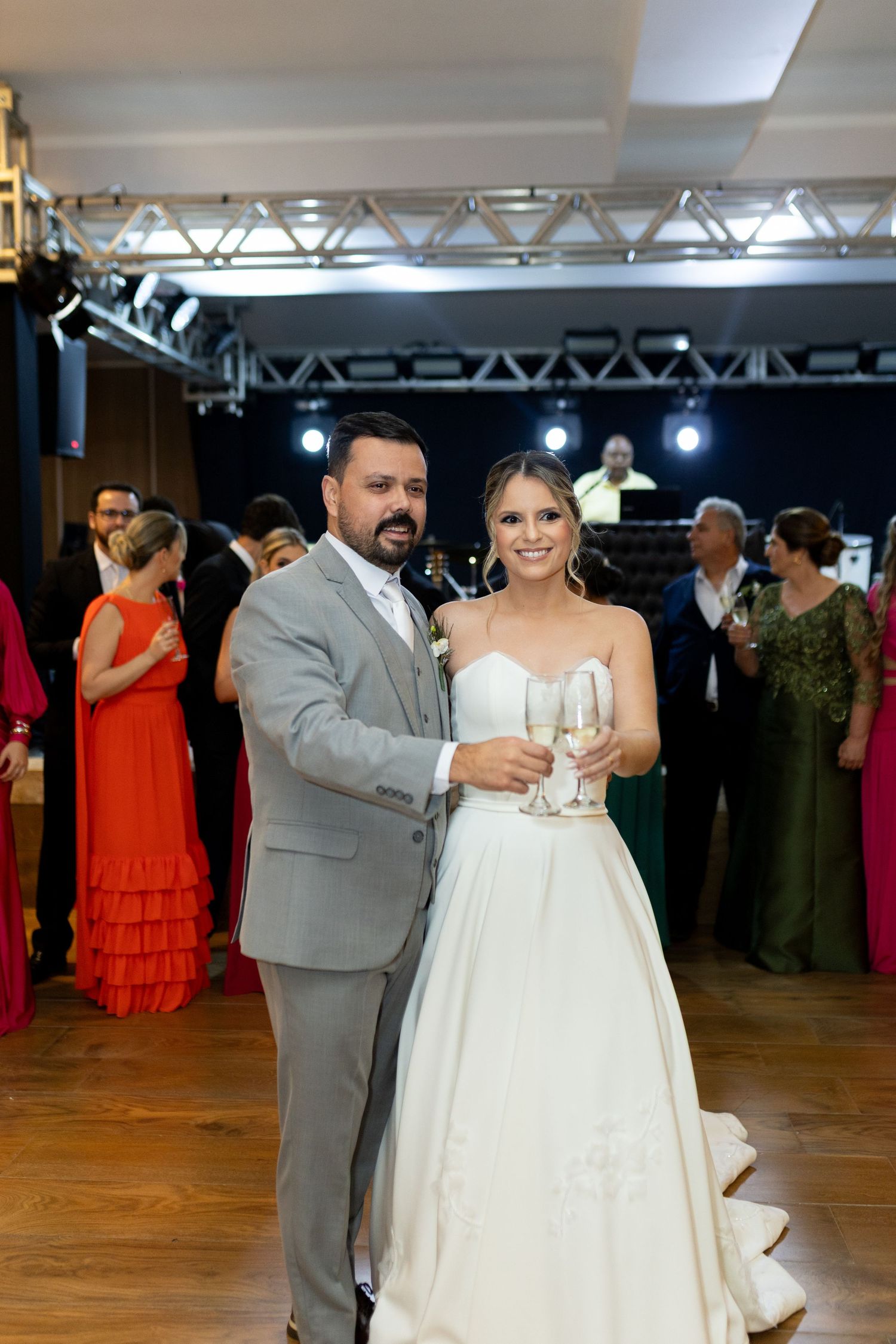 Bride in white gown and groom in gray suit toast with champagne glasses at elegant wedding reception.