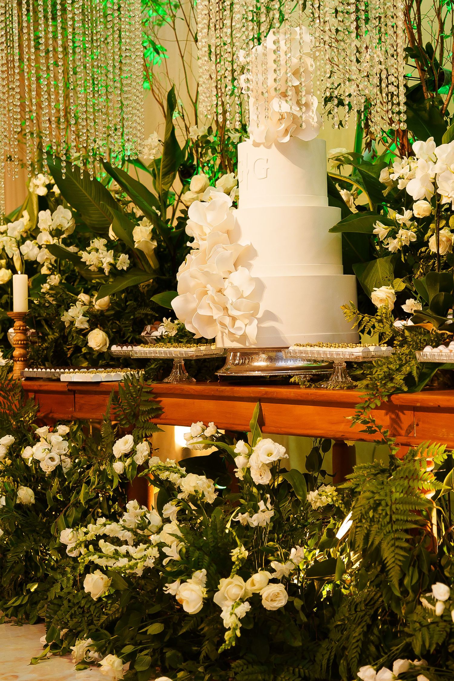 Elegant white tiered wedding cake adorned with orchids, surrounded by lush greenery and white flowers on a decorated table.