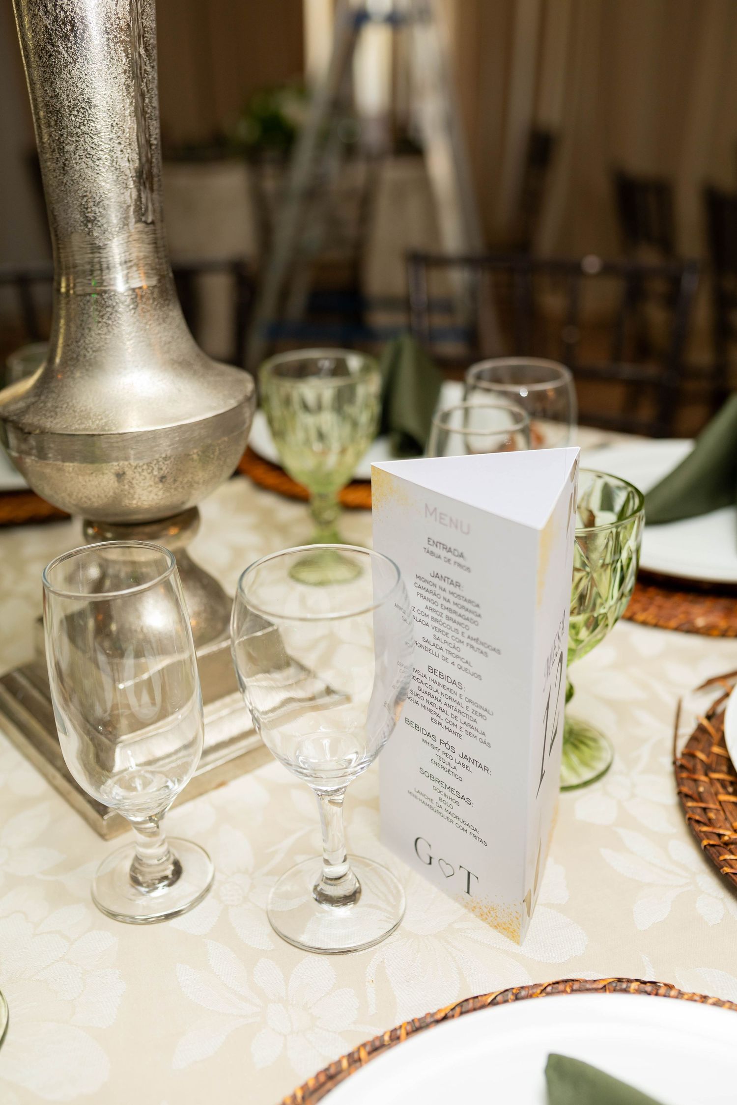 Elegant wedding table setting with menu card, crystal glasses, green goblets, and silver vase on white linen.