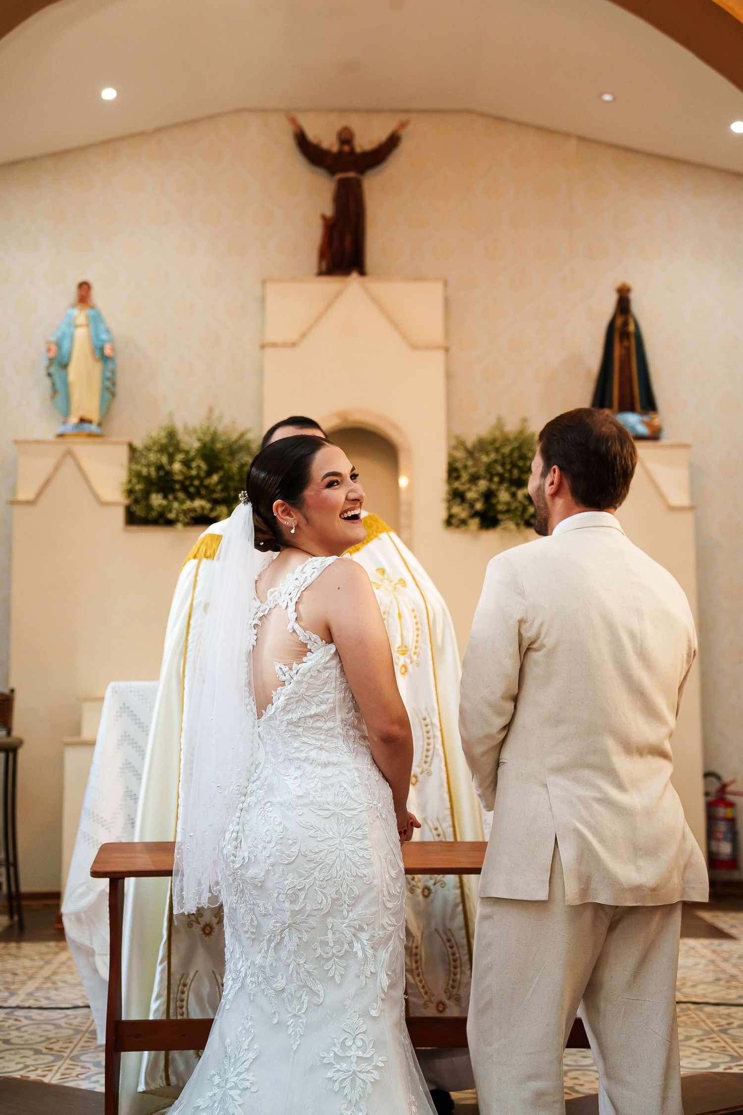 Smiling bride in lace gown turning back during Catholic wedding ceremony at church altar.