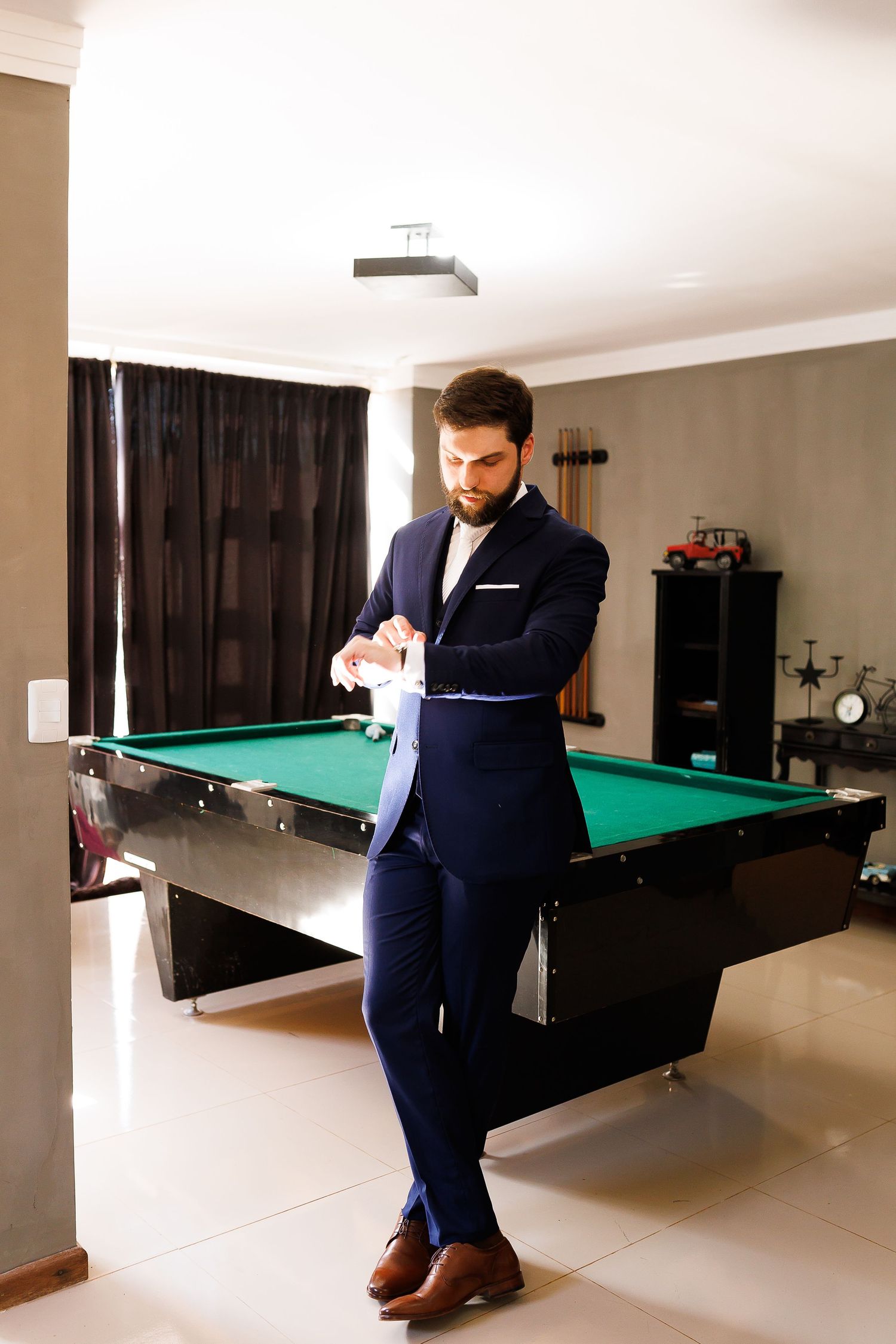 Stylish man in navy blue suit leaning against green pool table in elegant billiards room.