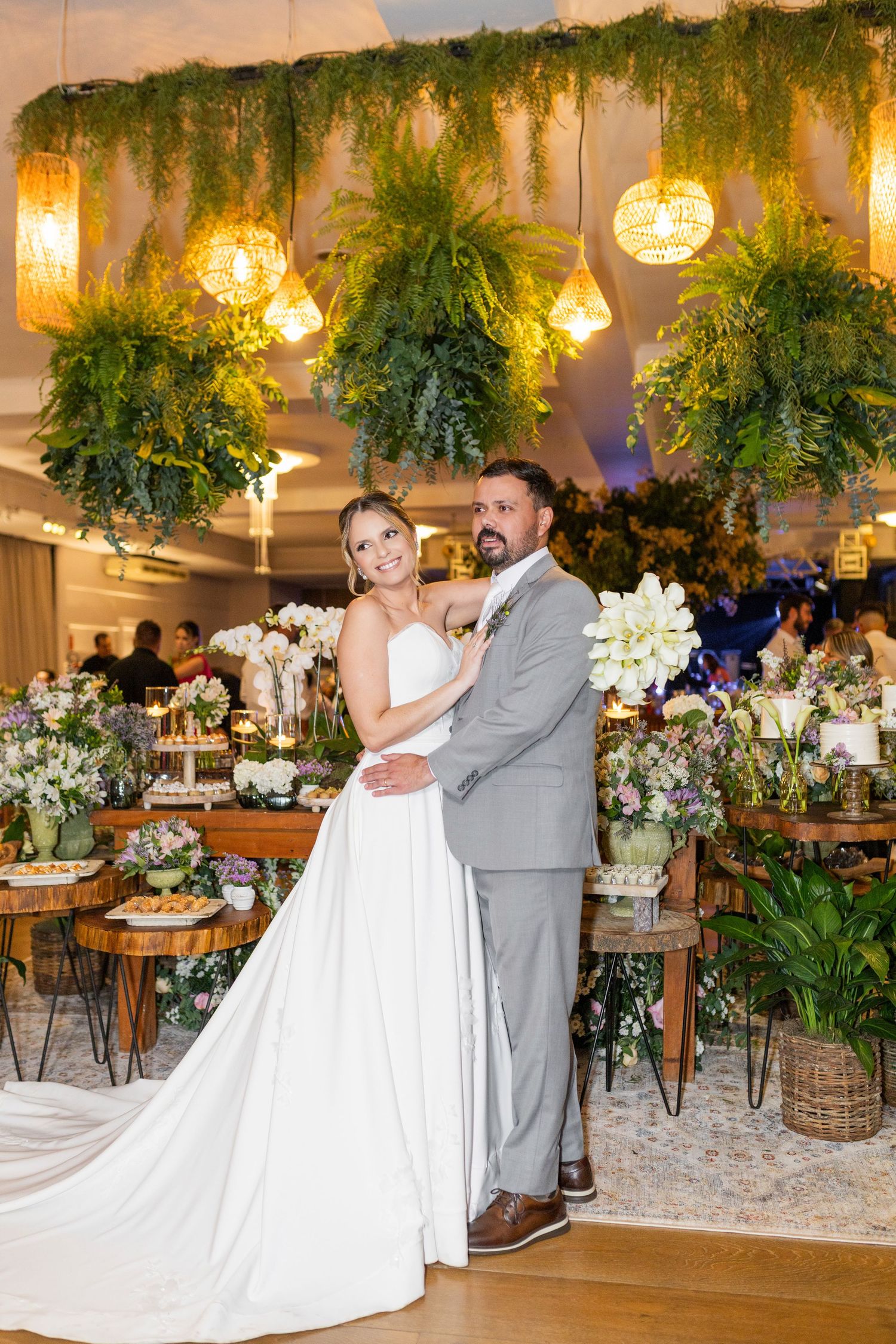 Bride and groom pose elegantly under lush greenery and golden lights at a beautifully decorated wedding reception.