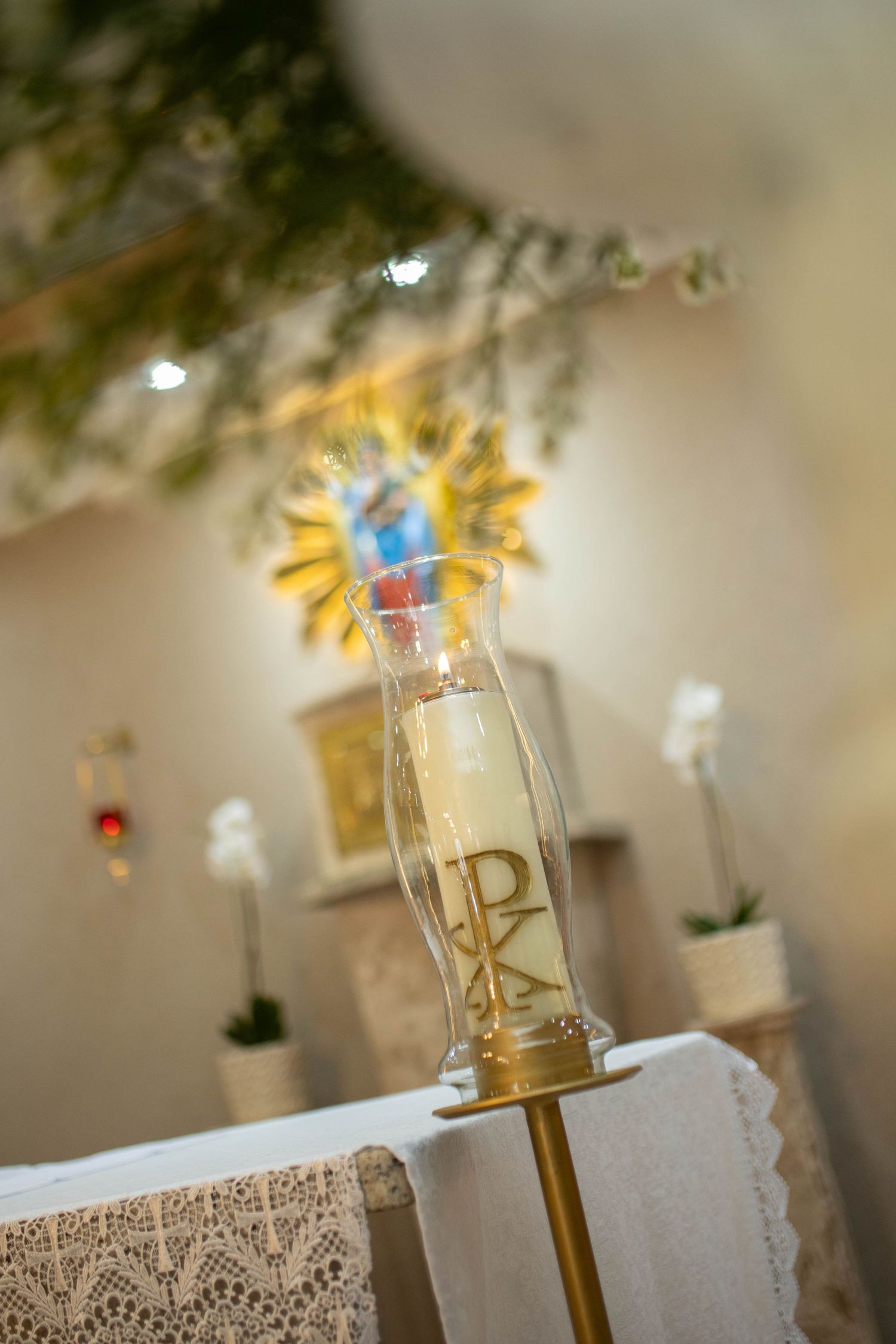 Chi Rho symbol on a glass candle holder at a Catholic church altar with white flowers and decorations.