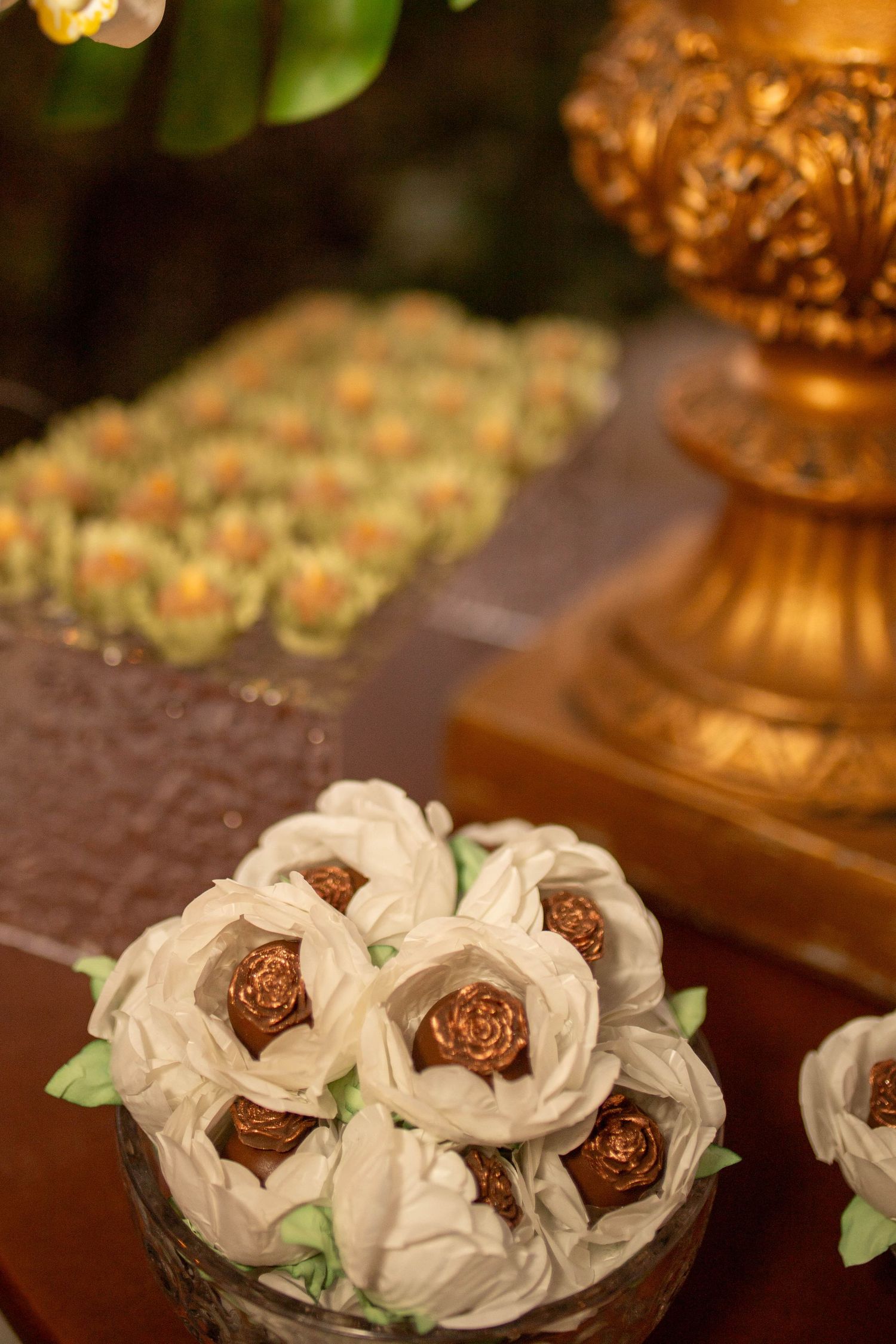 Elegant white and gold chocolate flower candies displayed in a glass bowl at a luxury wedding dessert table.