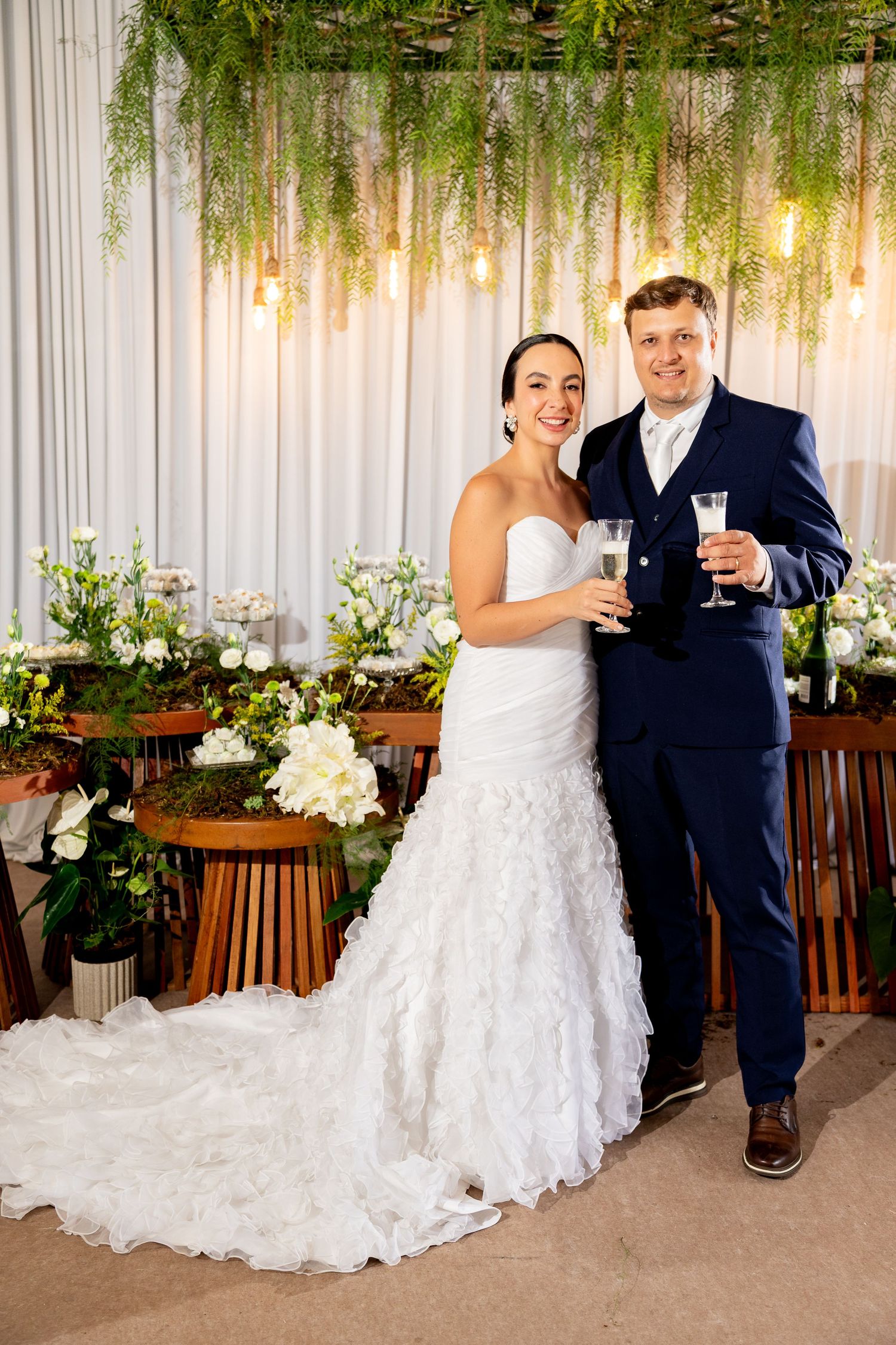 Bride and groom toasting with champagne glasses at elegant wedding reception with floral decor and hanging lights.