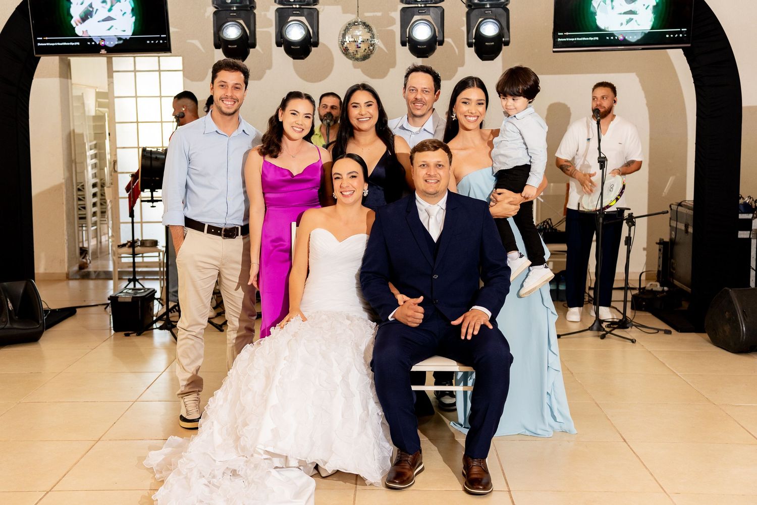 Bride and groom pose with wedding guests and live band in elegant venue.