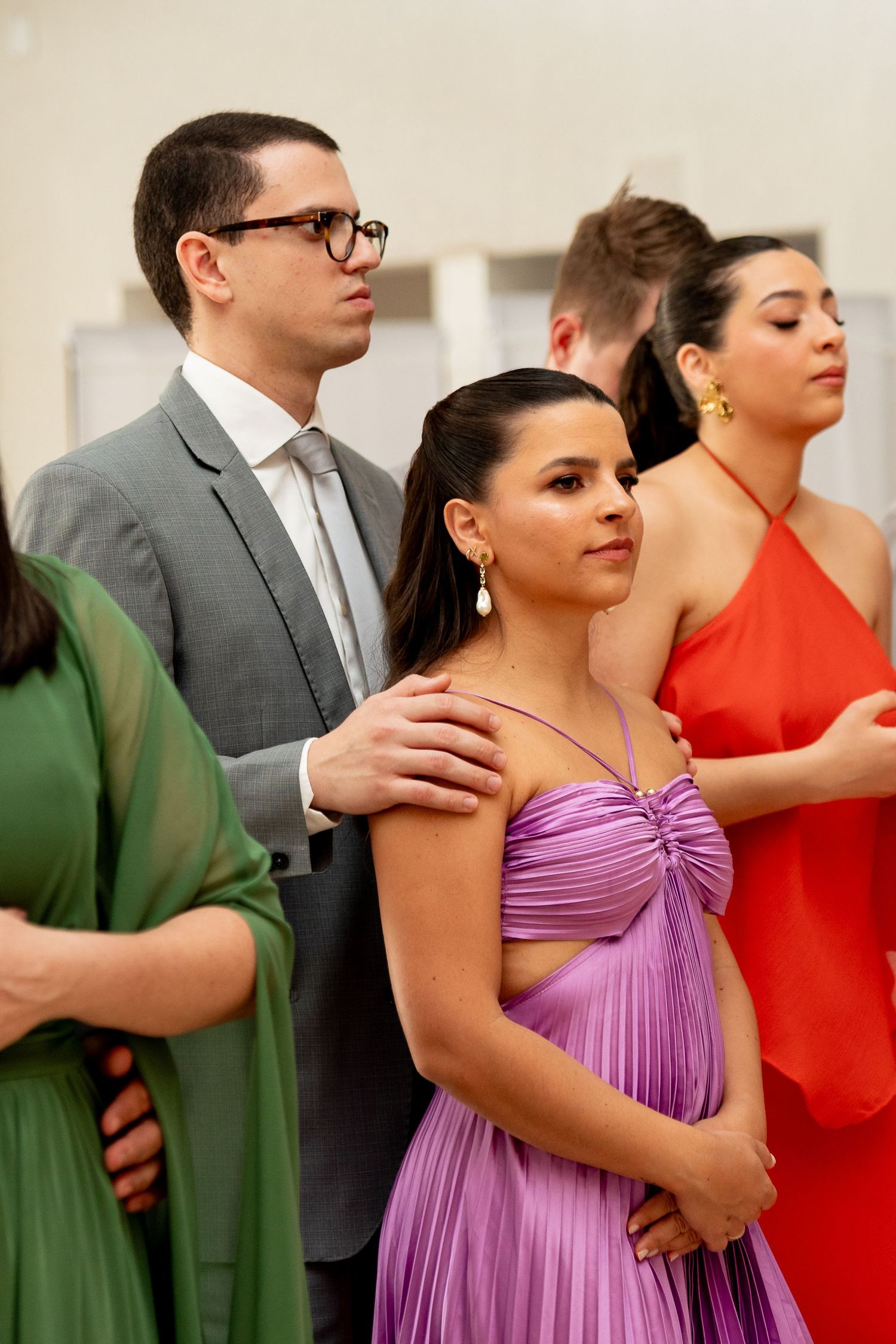 Elegantly dressed guests at a formal event, woman in purple gown with man in gray suit and woman in red dress.