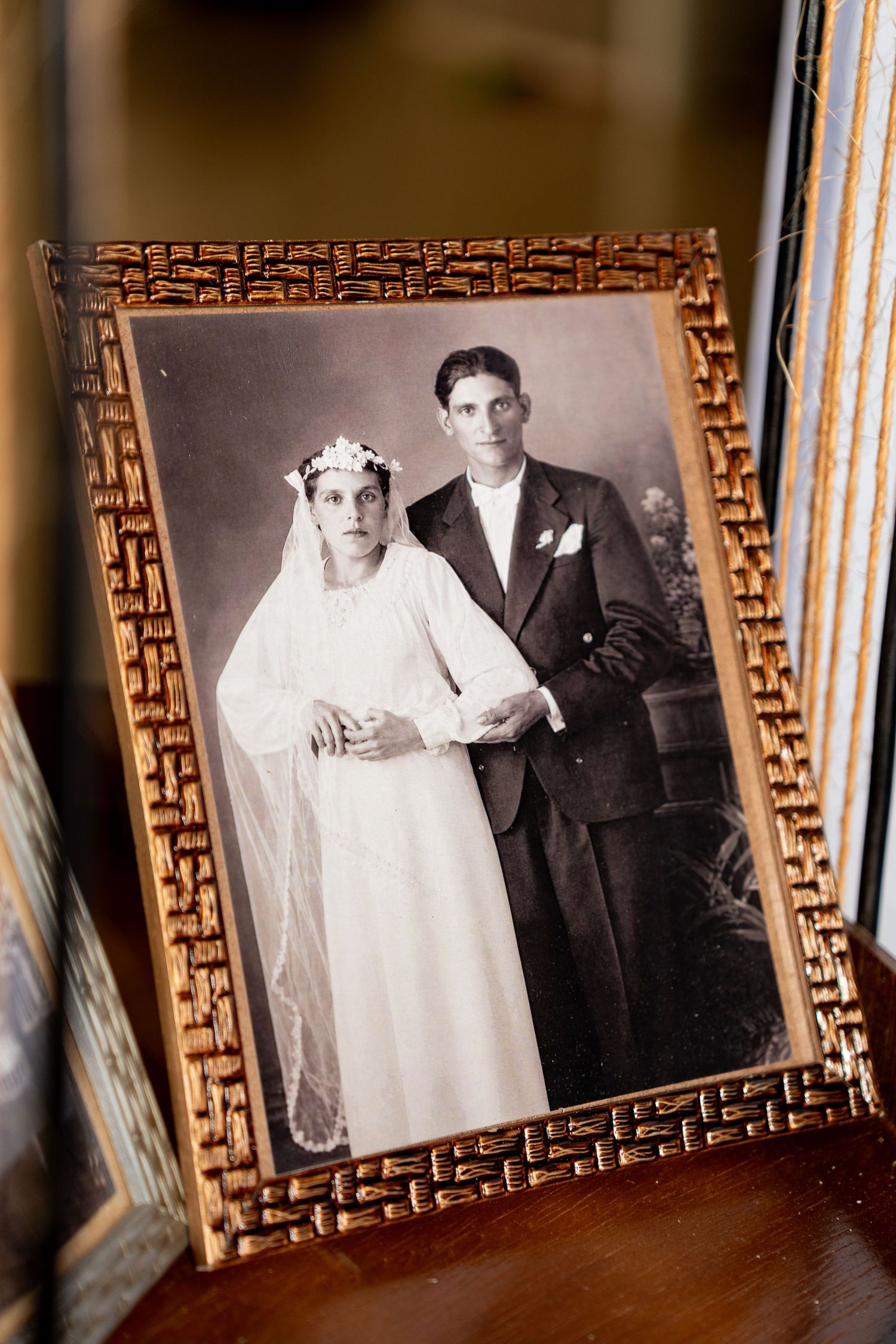 Vintage black and white wedding portrait in ornate gold frame showing bride in white gown and groom in dark suit.