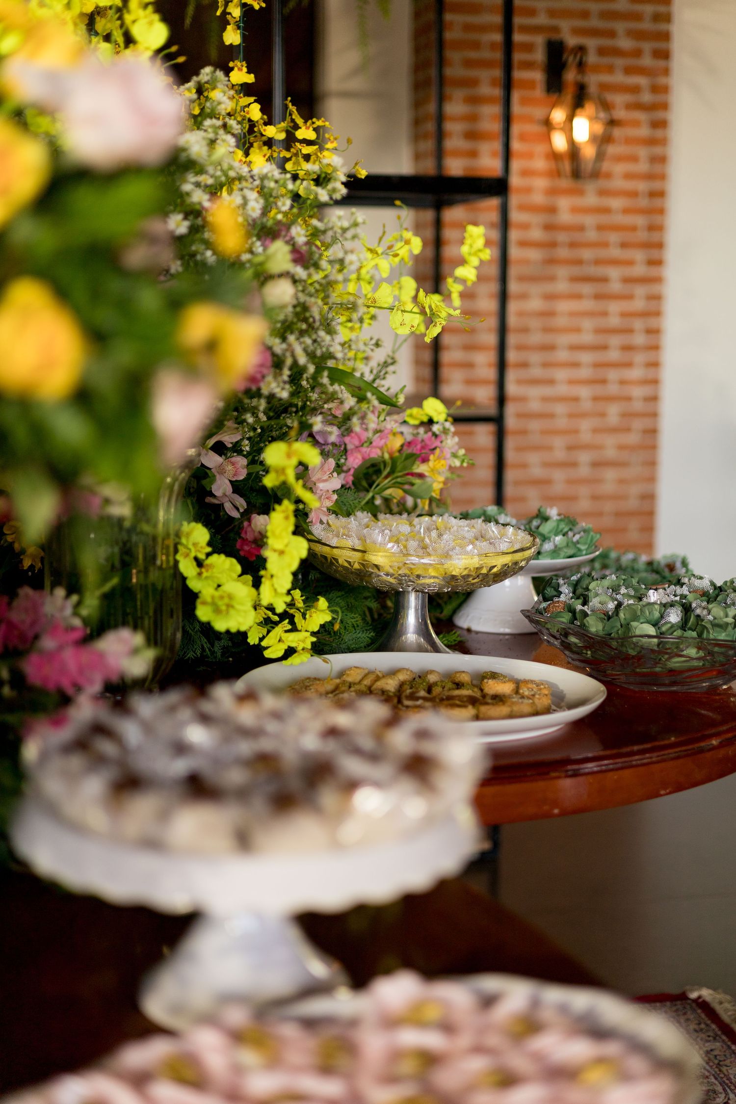 Elegant dessert table with colorful floral arrangements, assorted pastries, and decorative cake stands at an outdoor event.