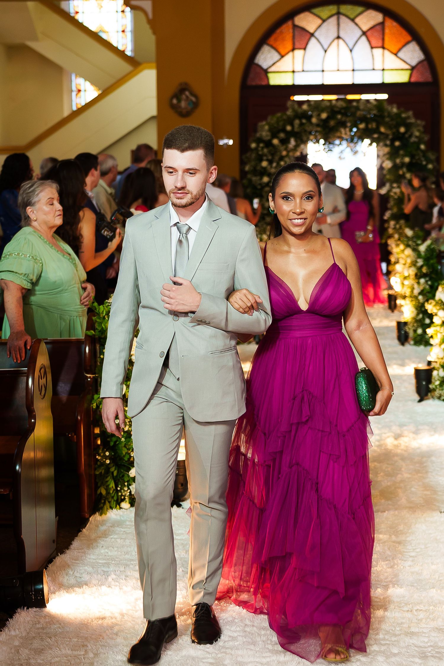 Elegant couple walking down aisle, man in gray suit, woman in vibrant purple gown at formal event.