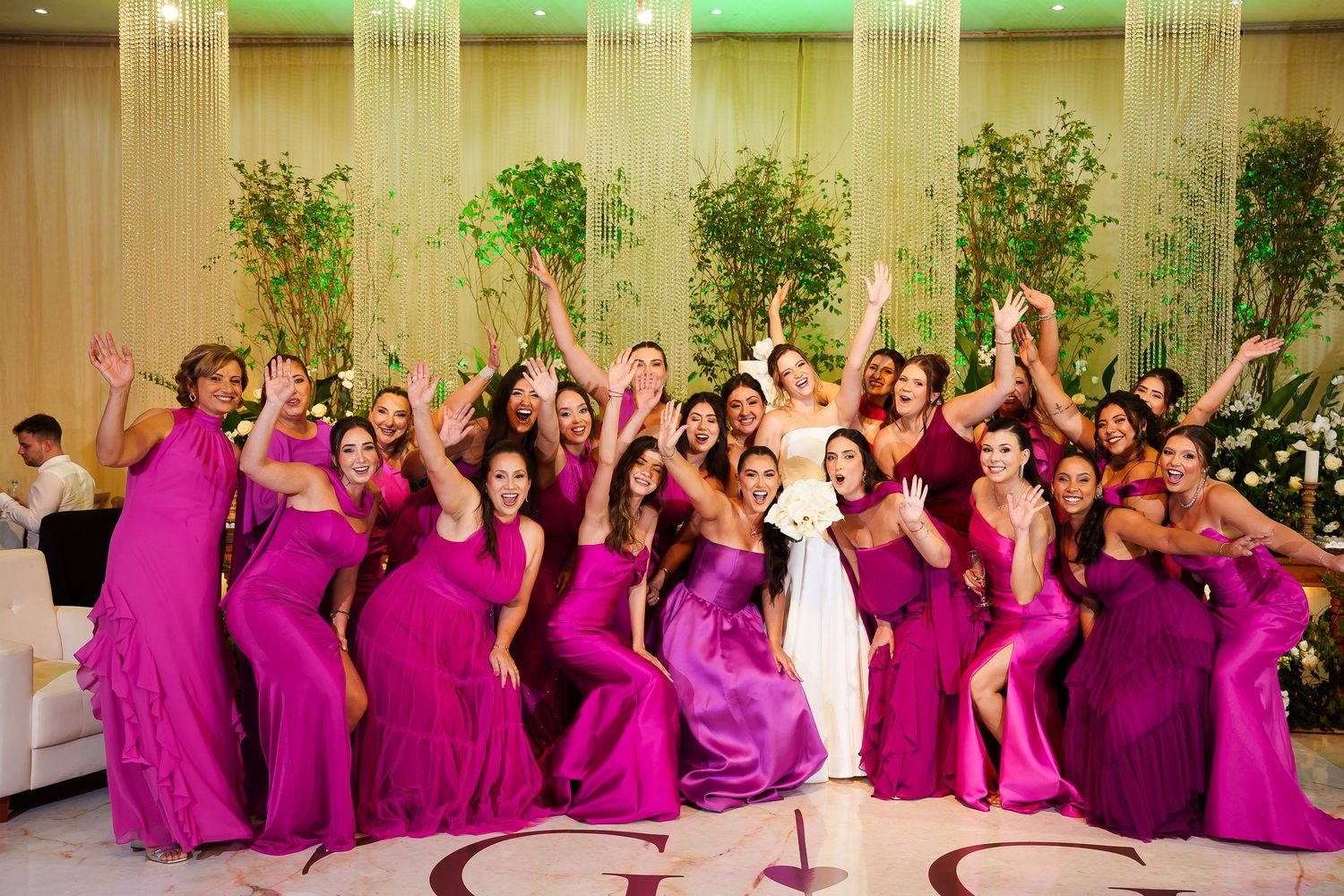 Bride surrounded by bridesmaids in fuchsia gowns celebrating joyfully at elegant wedding reception.