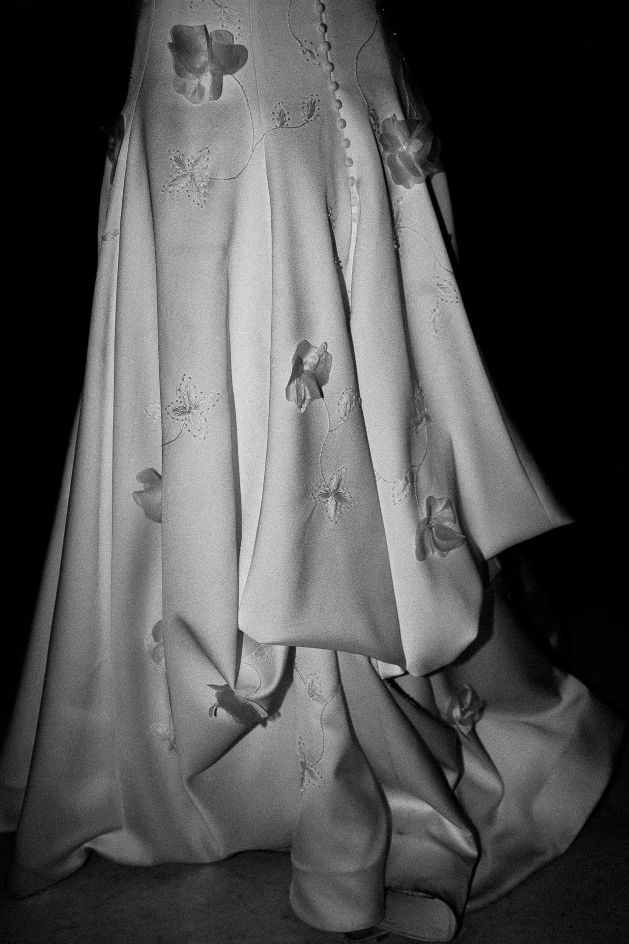 Black and white photo of an elegant floral appliqué ball gown skirt with dramatic draping and train.