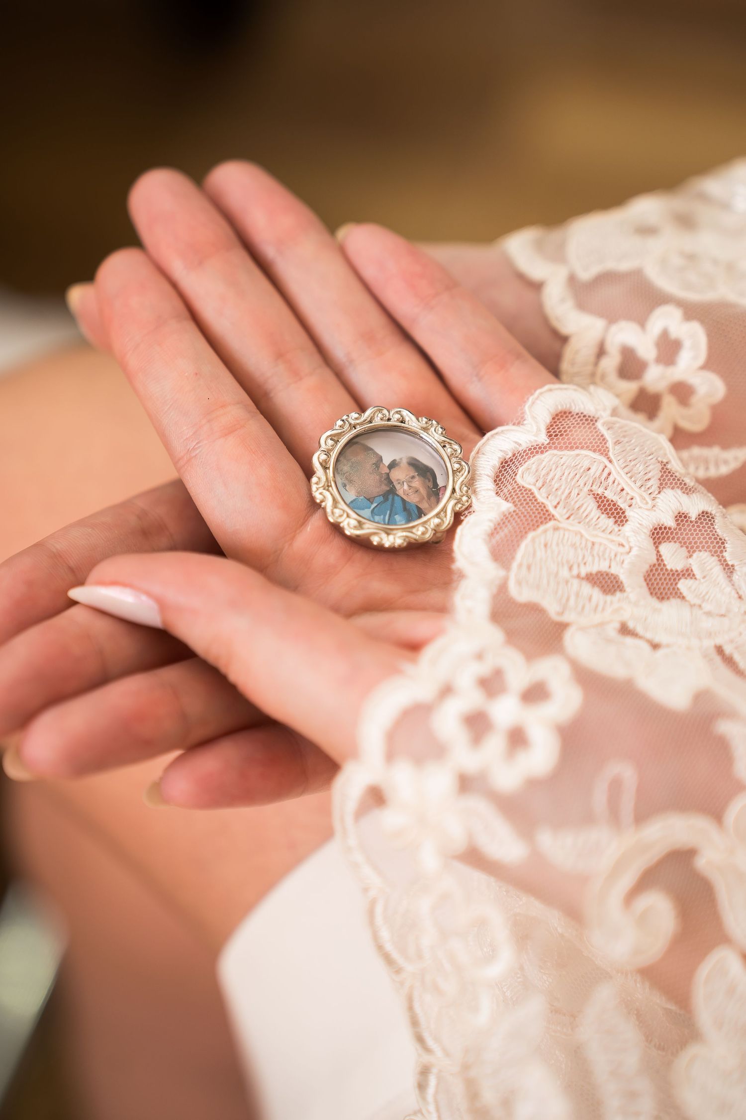 Bride holding a vintage locket with a portrait photo, wearing white lace wedding dress sleeve.
