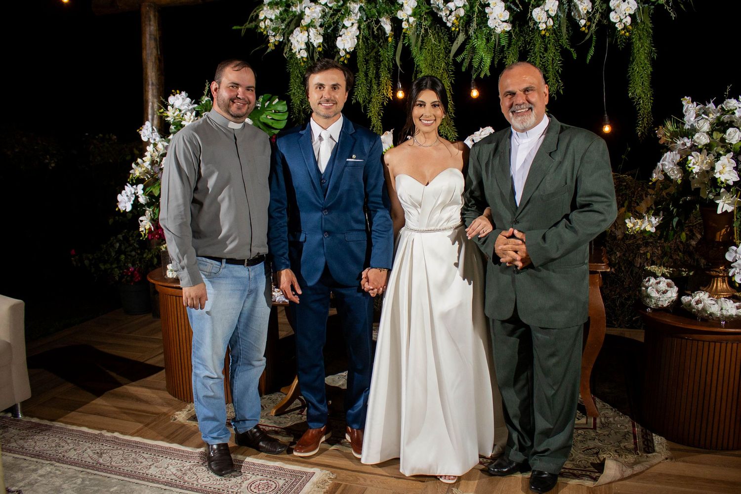 Bride and groom pose with two guests at an elegant outdoor wedding reception decorated with white flowers.