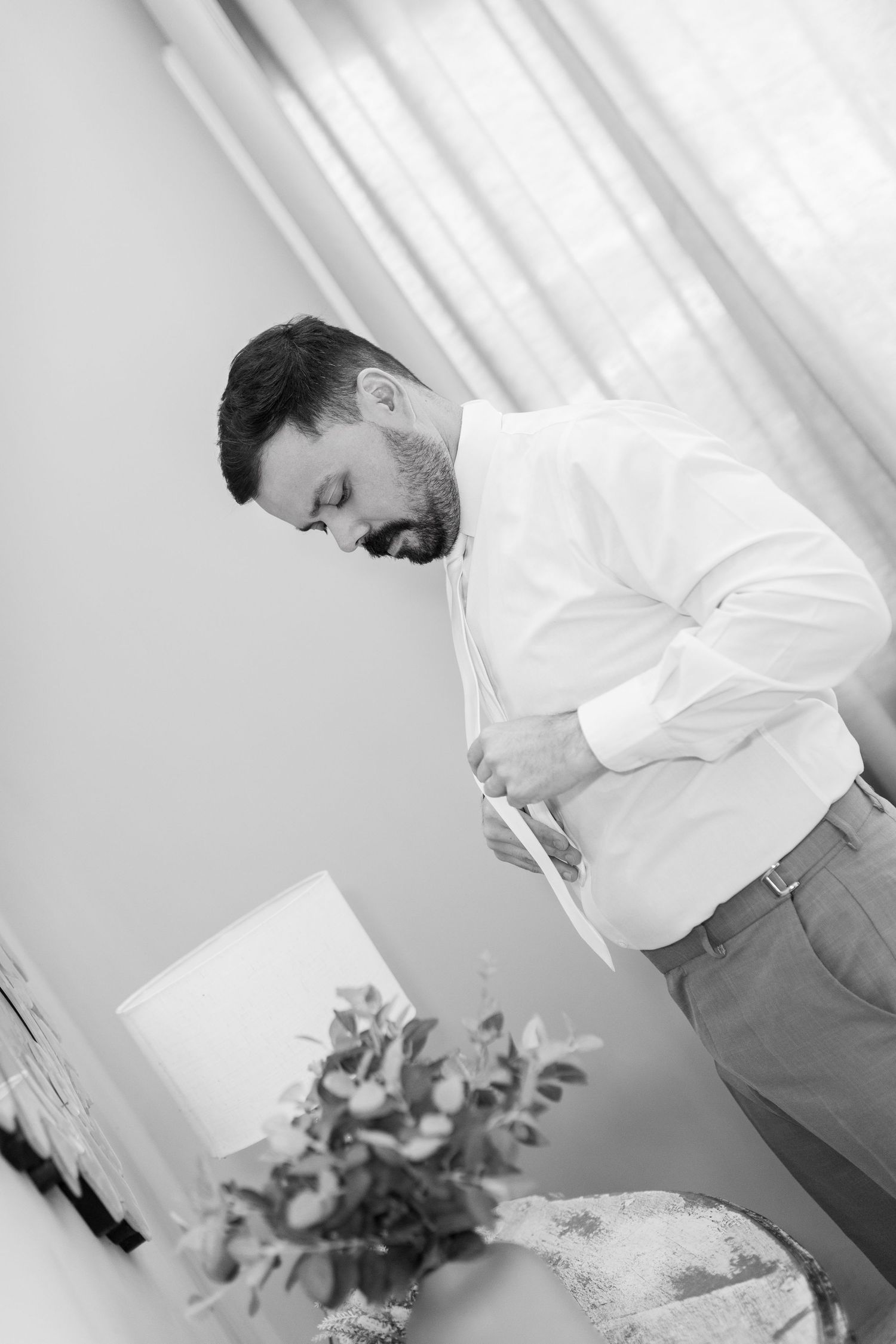 Black and white photo of a bearded man in a white shirt looking down at papers near a floral arrangement.
