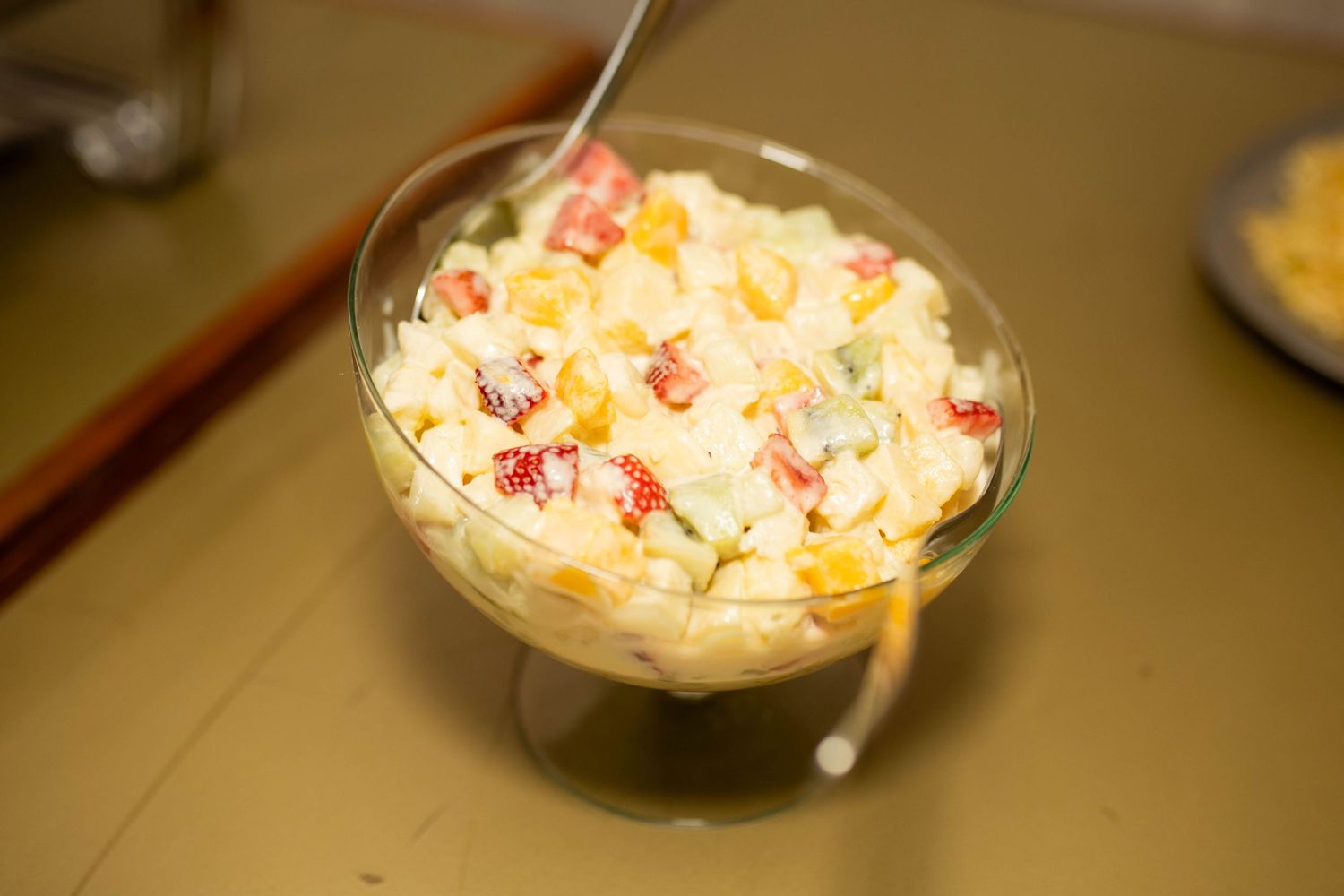 A glass bowl filled with creamy corn and crab salad, garnished with colorful vegetables, served with a spoon.