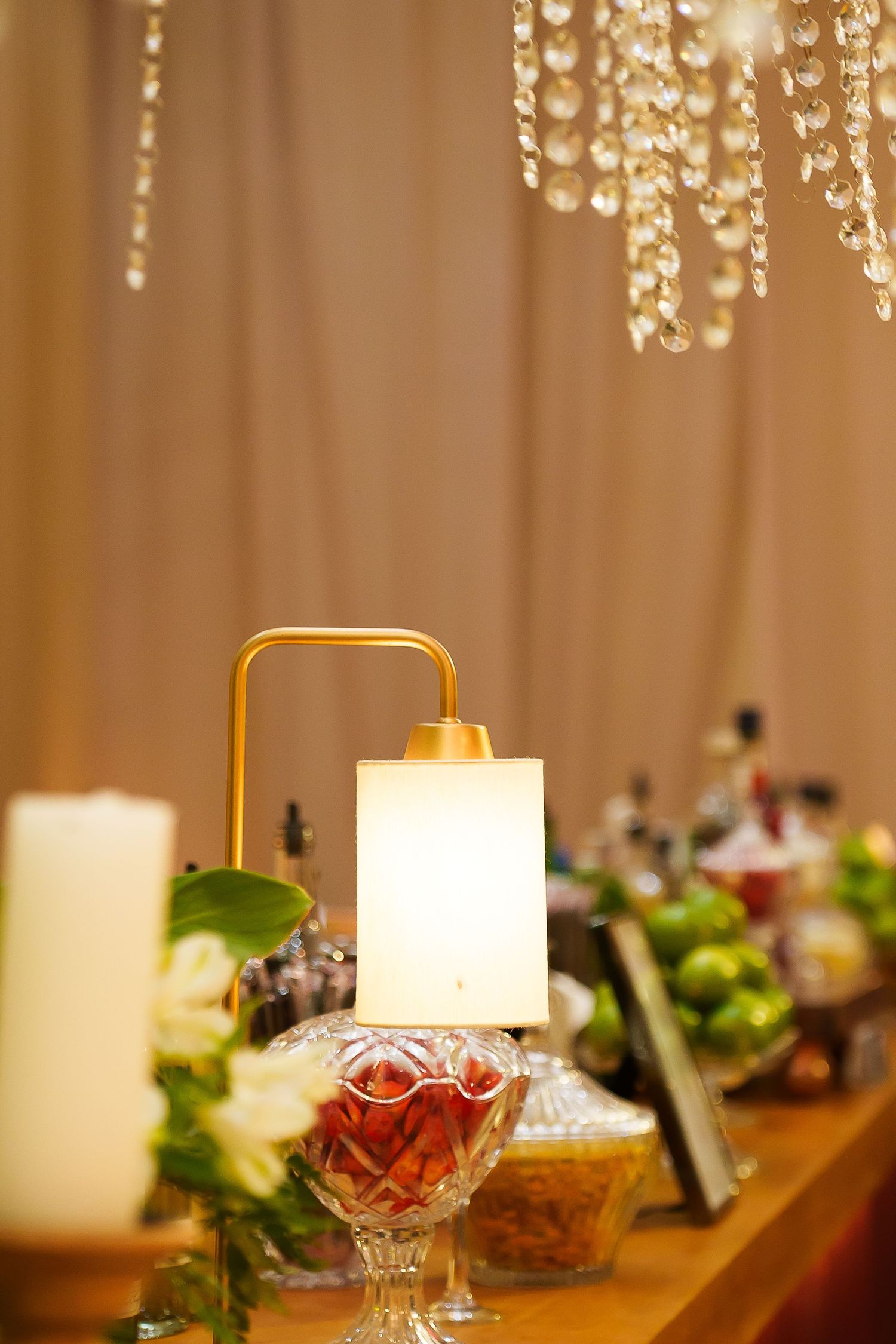Elegant table display with gold lamp, crystal bowl, white candles, and floral arrangement under a crystal chandelier.