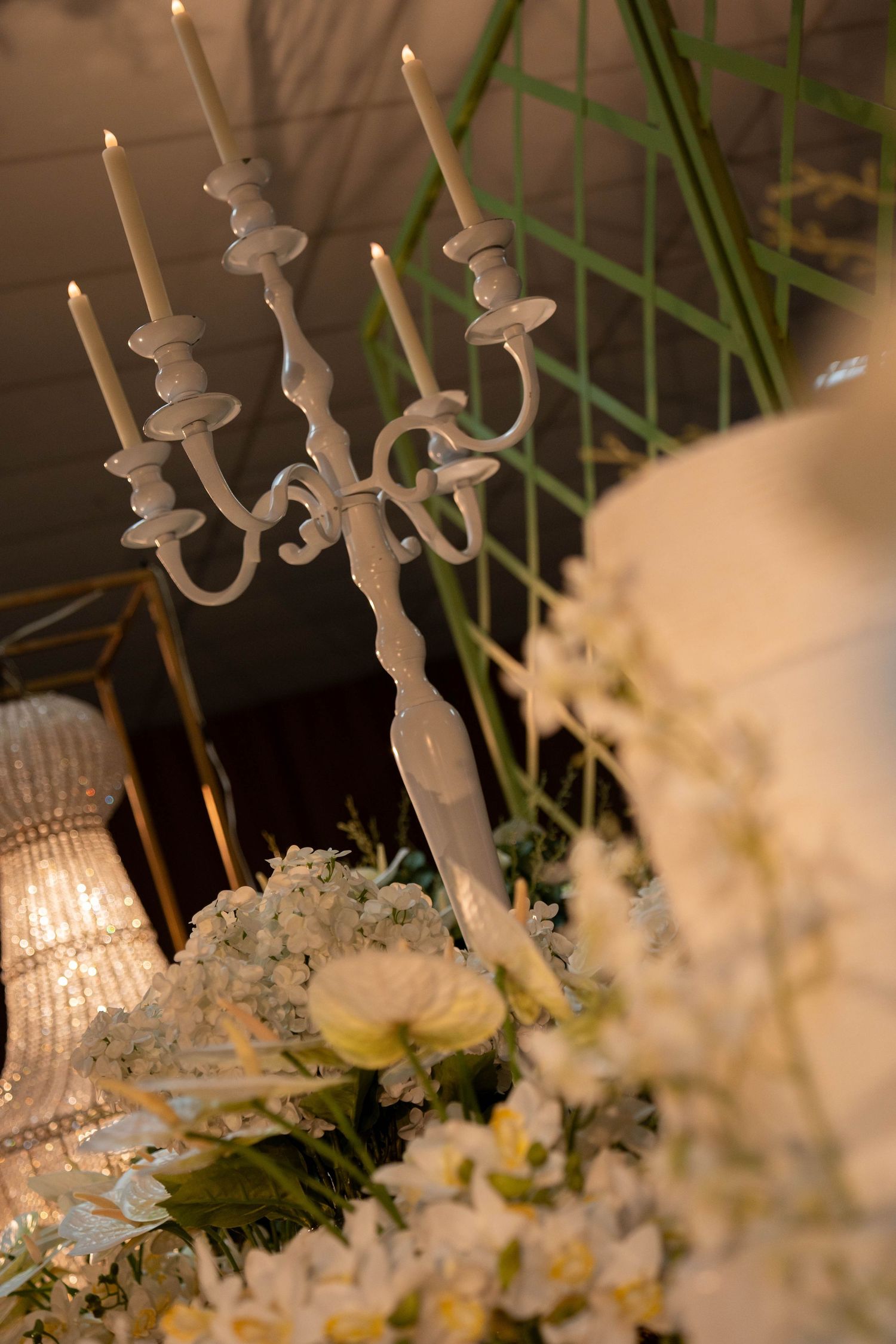 White candelabra with lit candles surrounded by white floral arrangements at an elegant wedding reception.