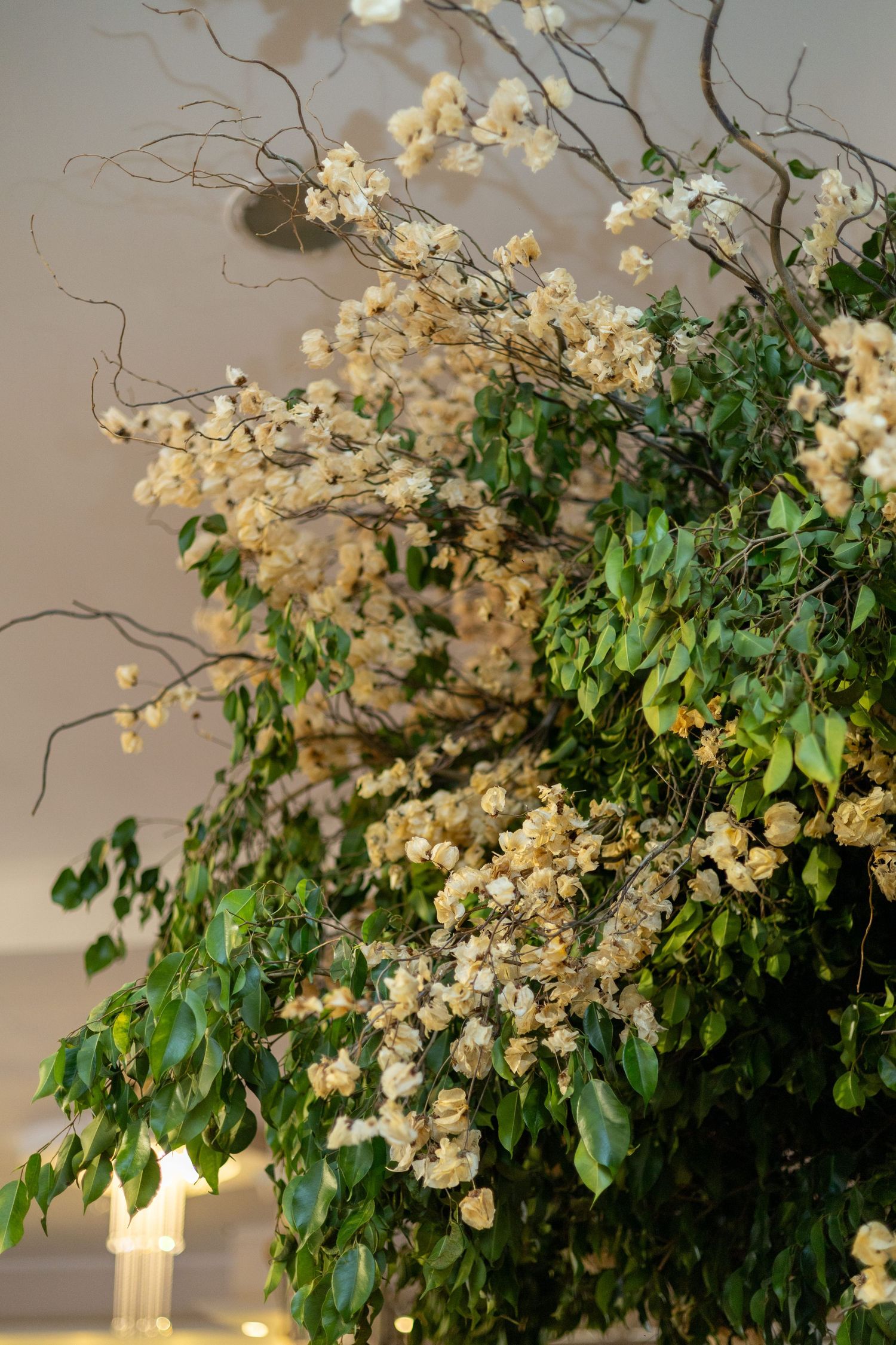 Elegant floral arrangement featuring white bougainvillea blooms and green leaves with decorative twisted branches.