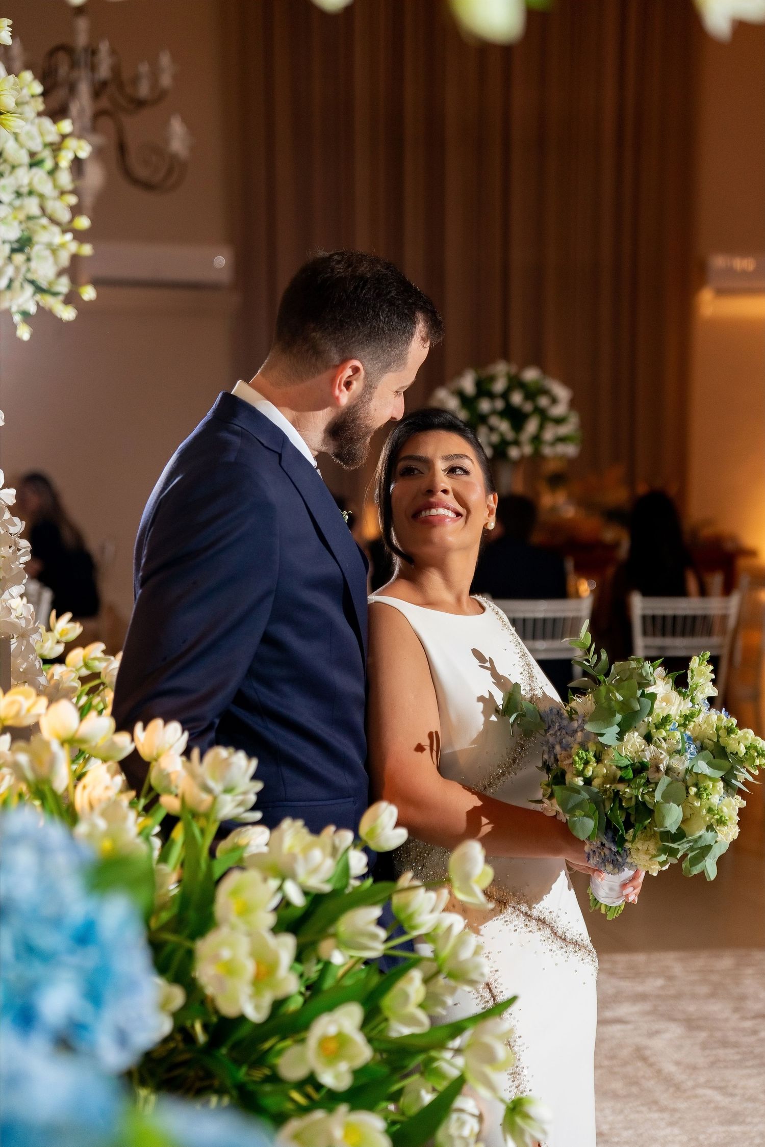 Bride and groom share a joyful moment surrounded by white and blue floral arrangements at their wedding ceremony.