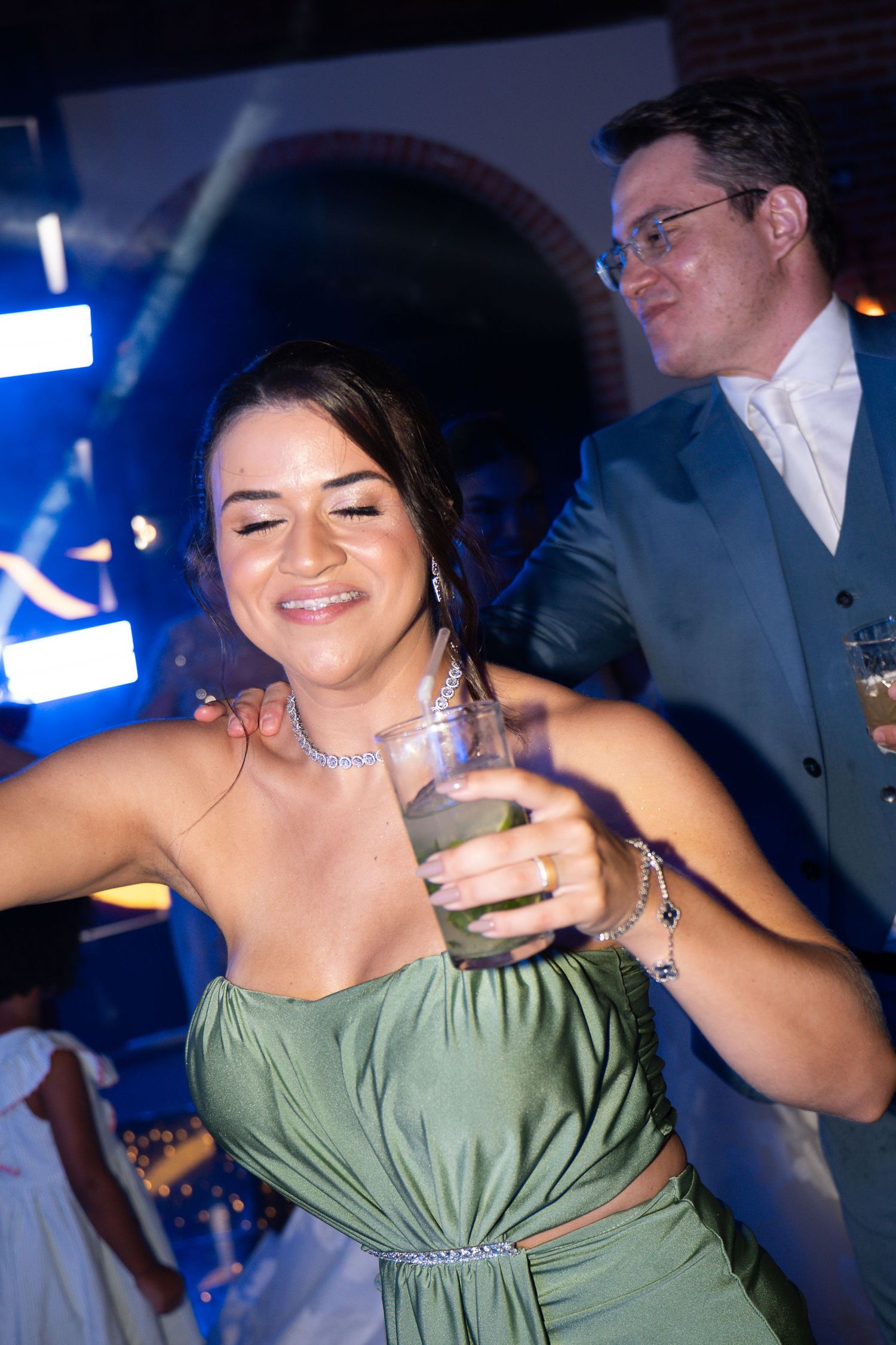 Woman in green dress dancing and holding a cocktail at an elegant evening wedding reception party.