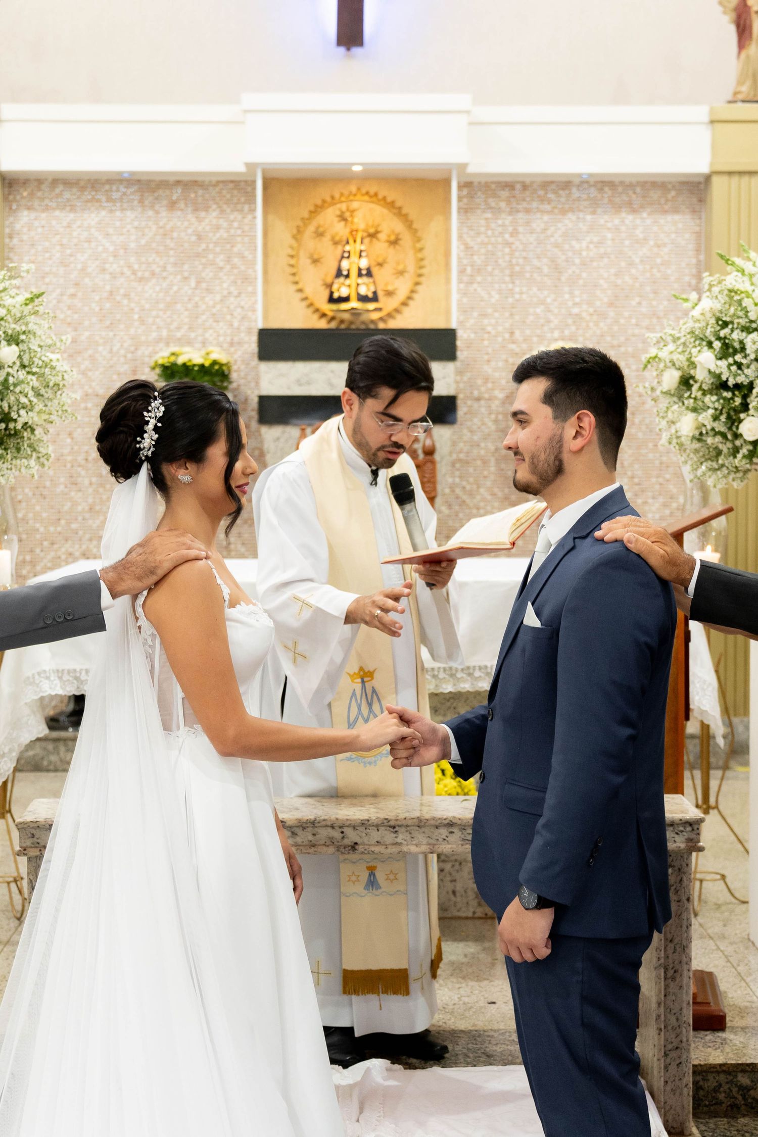Bride and groom exchange vows at church altar with priest officiating during elegant wedding ceremony.