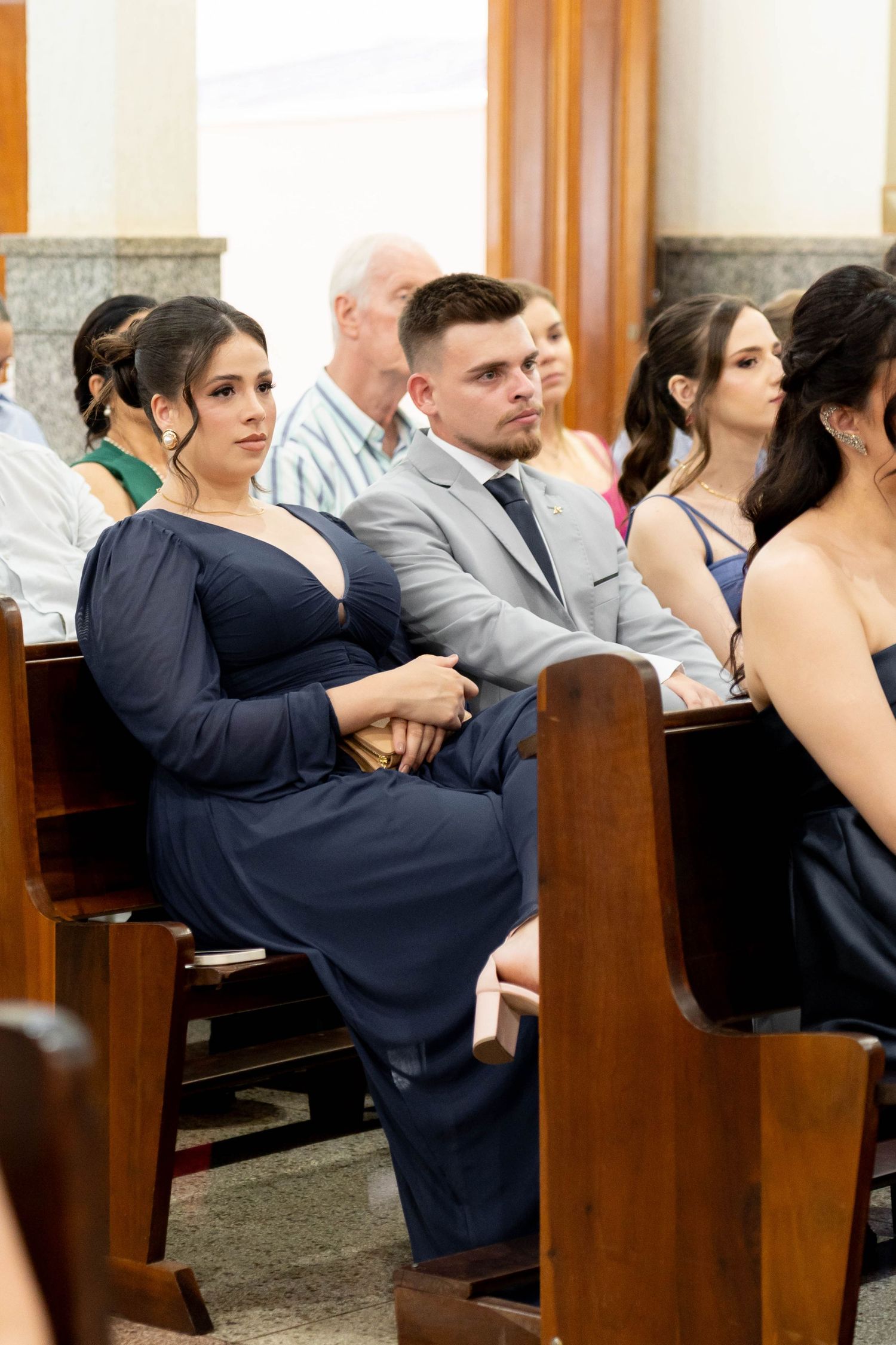 Guests seated in church pews during a wedding ceremony, wearing formal navy and gray attire.