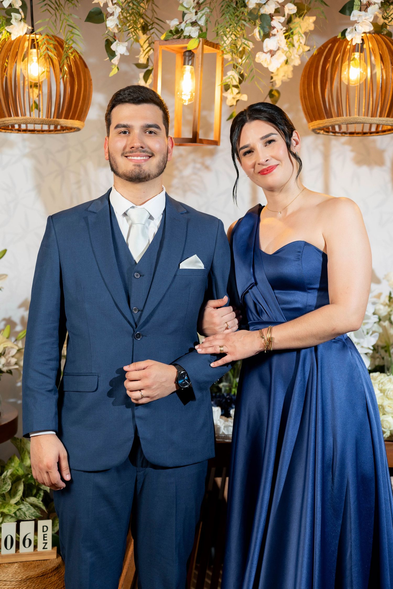Smiling couple dressed in coordinating navy blue suit and gown posing at a beautifully decorated venue.