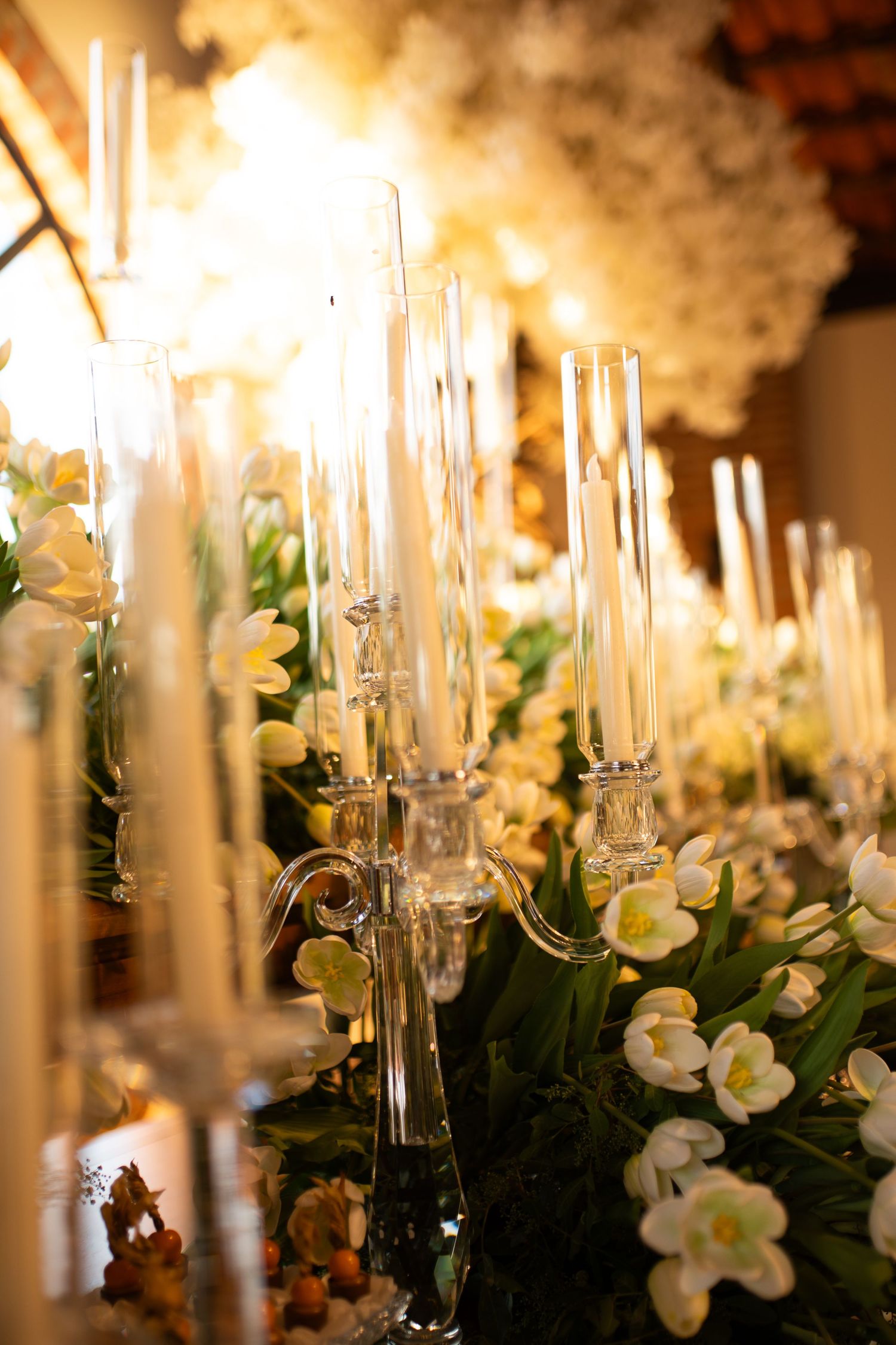 Elegant glass candelabras with white tulips and glowing candles create a luxurious wedding table centerpiece.