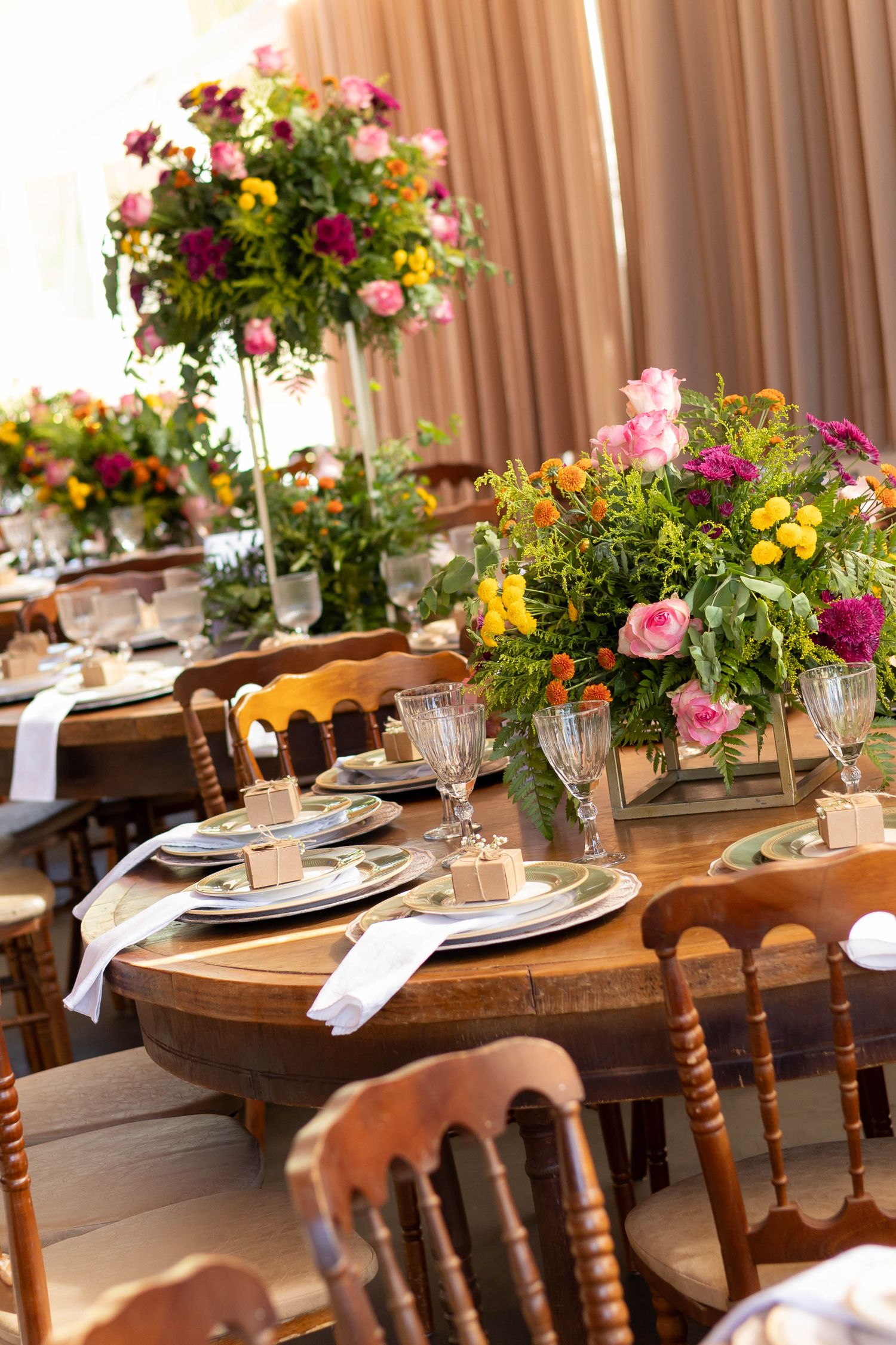 Elegant wedding reception table with colorful floral centerpieces, crystal glasses, and place settings on rustic wooden tables.