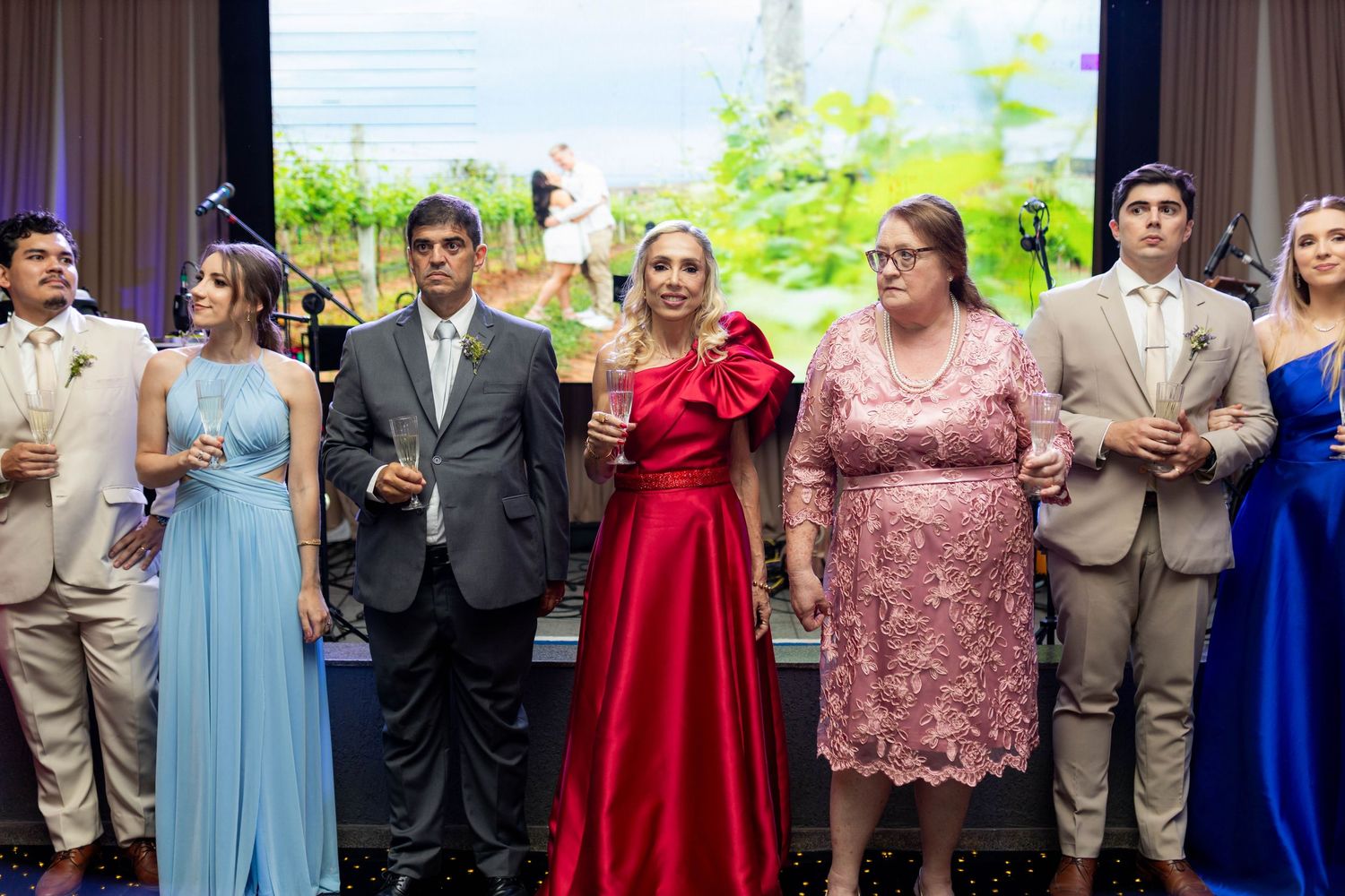 Elegantly dressed guests at a formal event, featuring women in red and blue gowns and men in suits.
