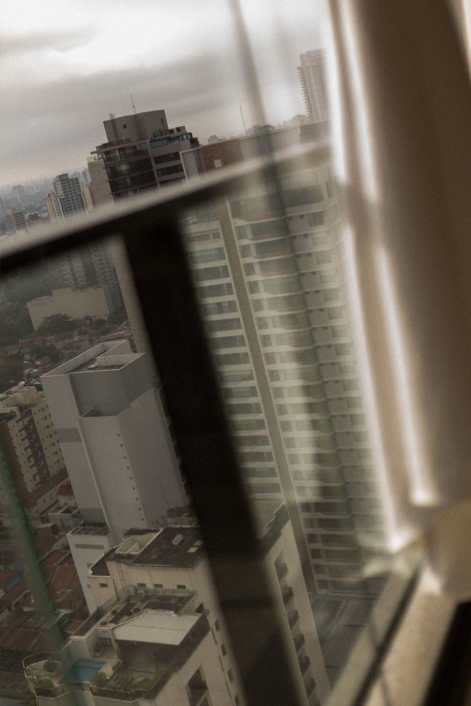 Aerial city view through a glass window showing modern skyscrapers under overcast skies.