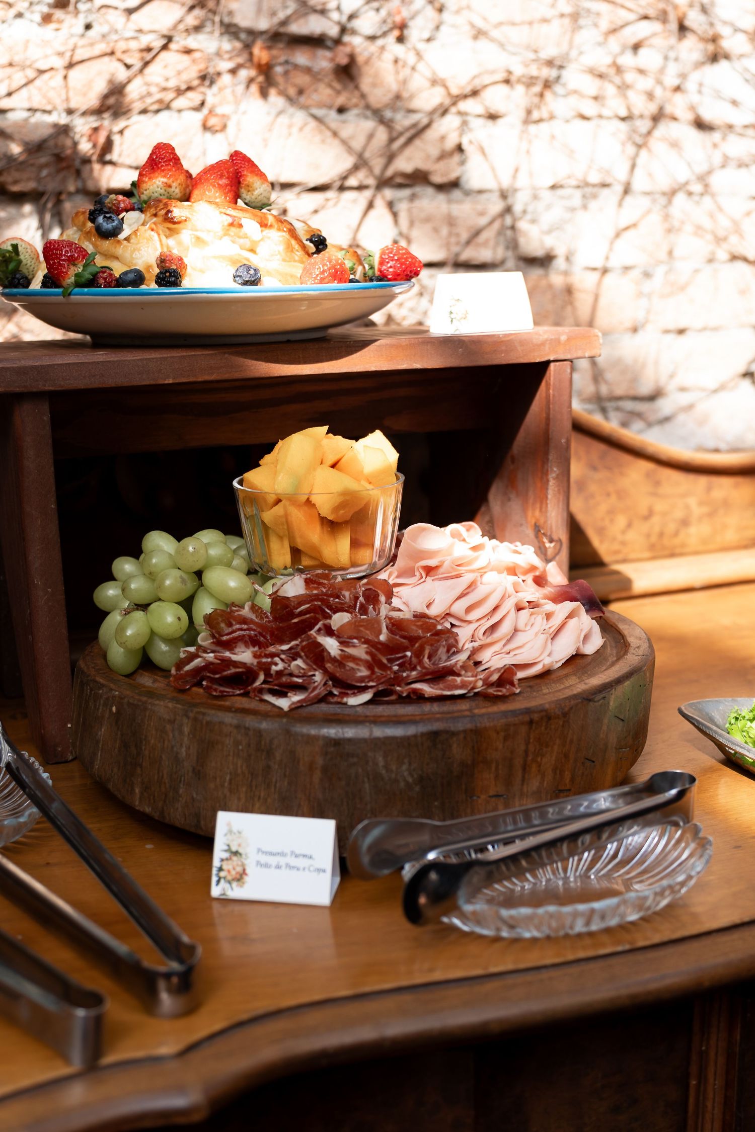 Elegant charcuterie board with sliced meats, green grapes, and melon, displayed on a wooden platter at a buffet spread.