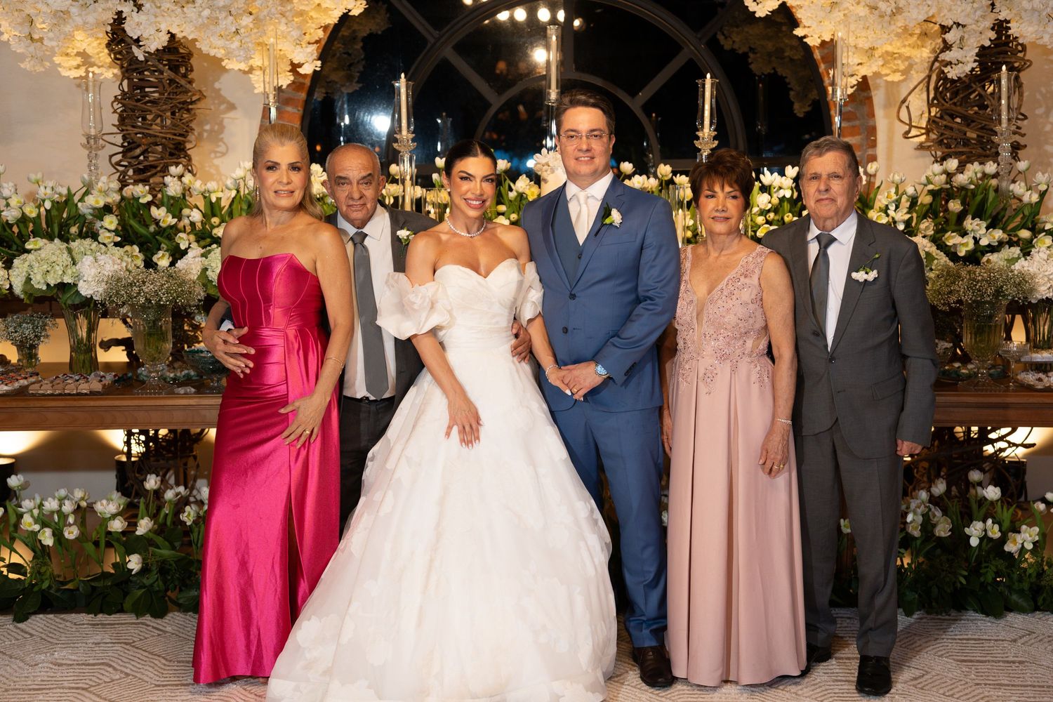 A bride and groom pose with family members in elegant formal attire at a beautifully decorated wedding venue.