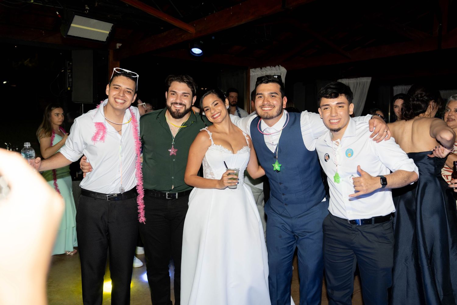 Bride in white dress poses with groom in blue suit and three friends at a festive wedding reception.
