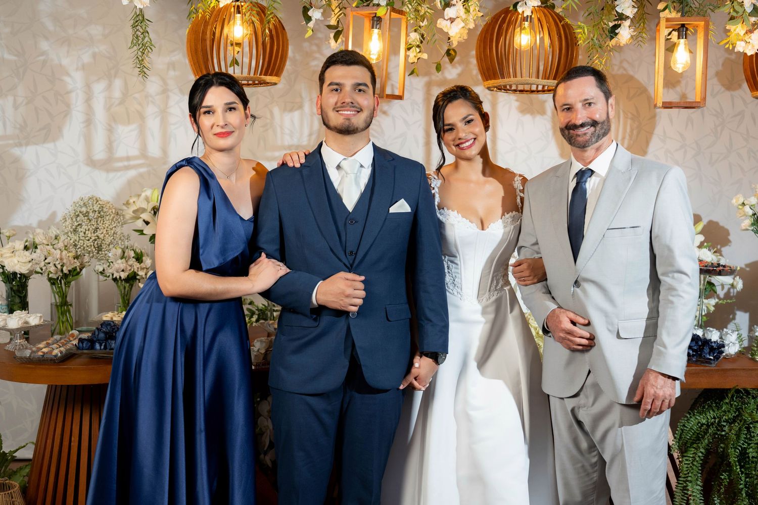 Elegant wedding party with bride in white gown, groom in navy suit, and guests in formal attire at decorated venue.
