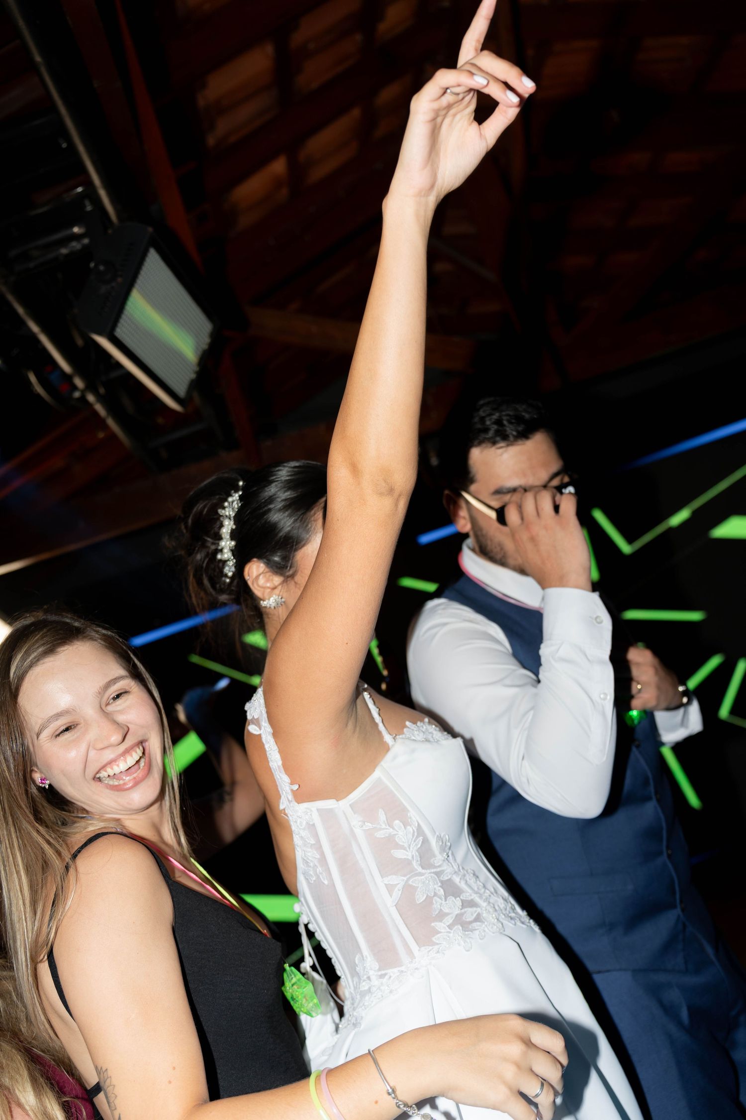 Bride in white dress dancing with arms raised at wedding reception with guests celebrating on dance floor.