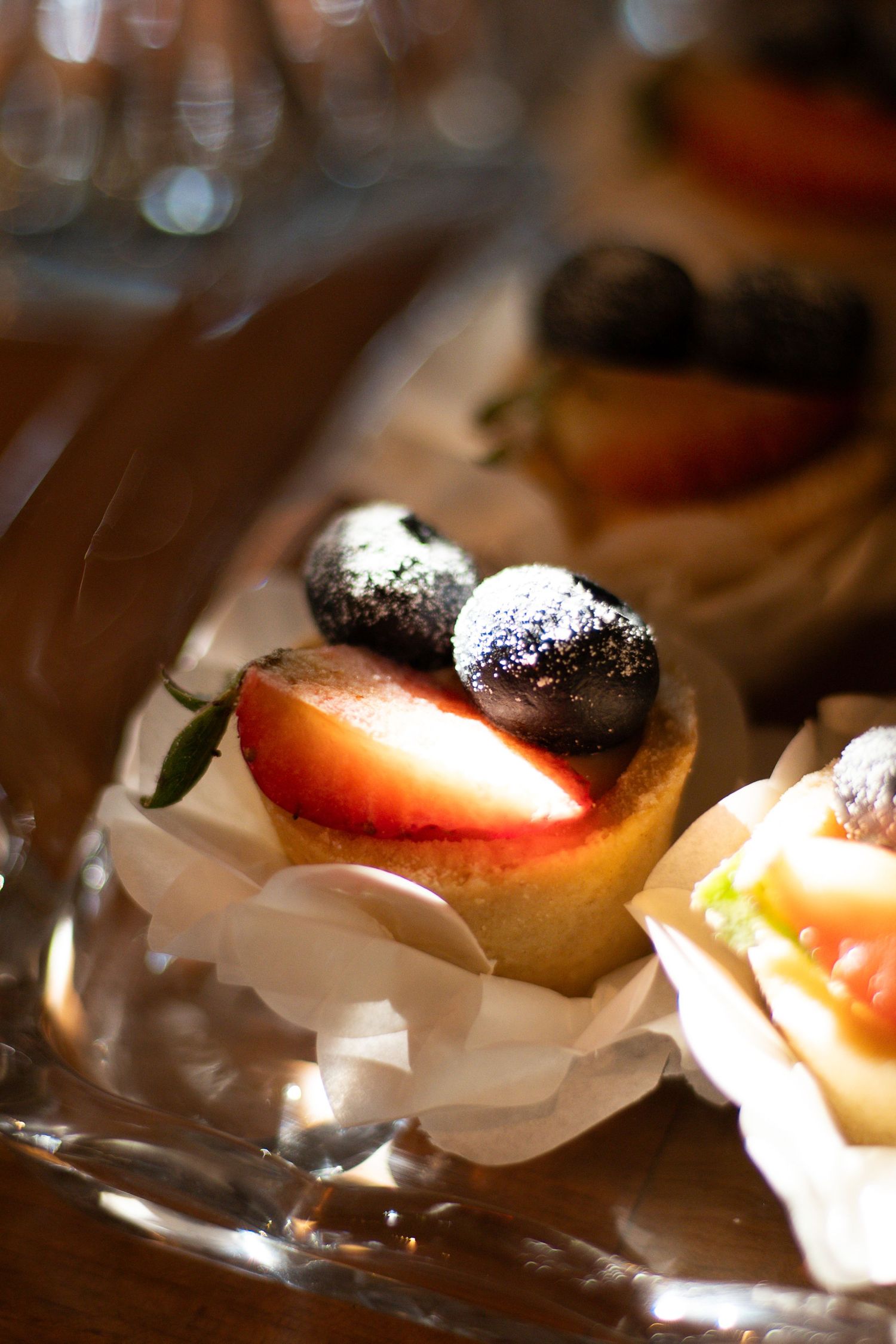 Elegant fruit tarts topped with blueberries and strawberry slices dusted with powdered sugar on a crystal platter.