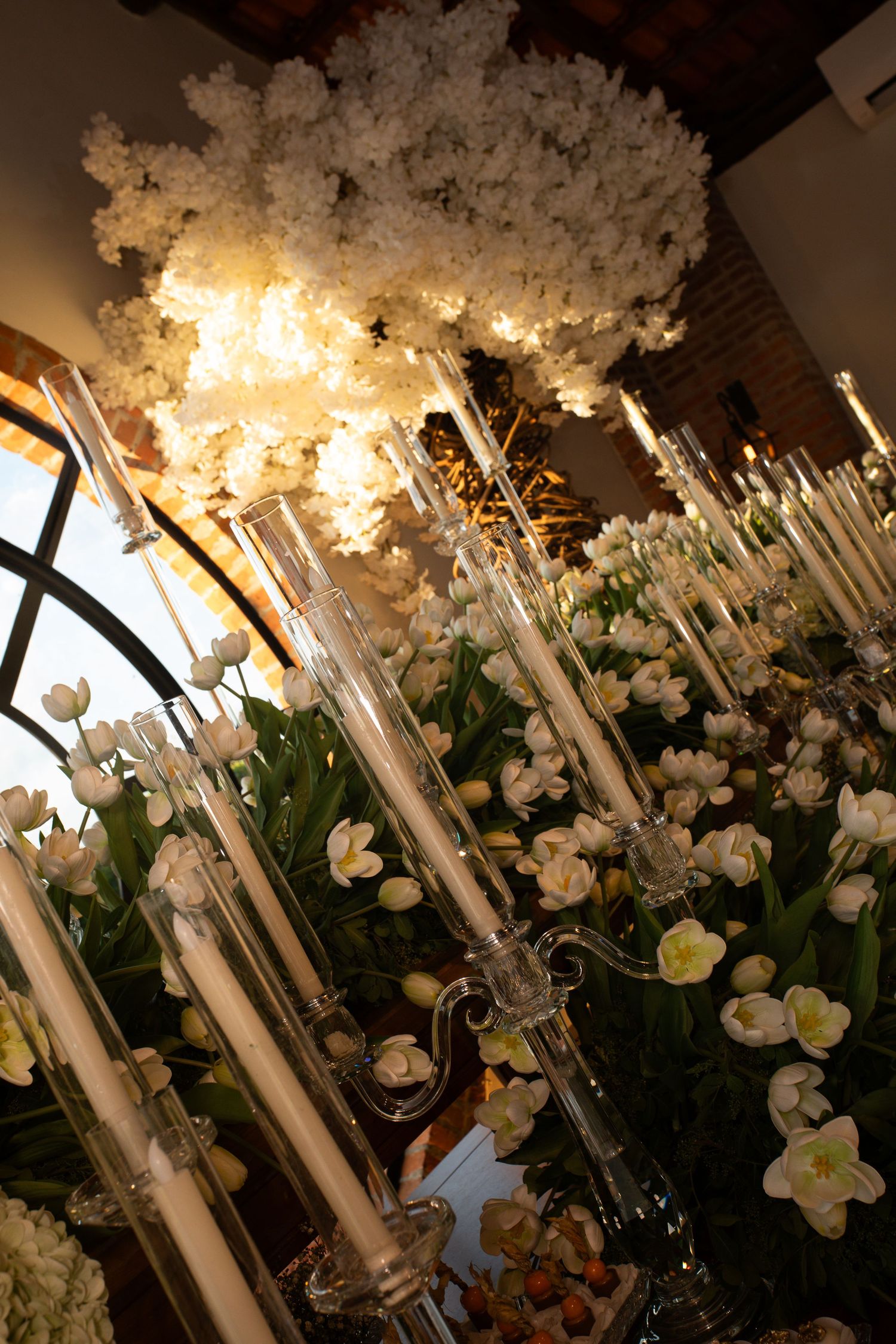 Elegant wedding decor with crystal candelabras, white tulips, and illuminated floral cloud centerpiece in a warmly lit venue.