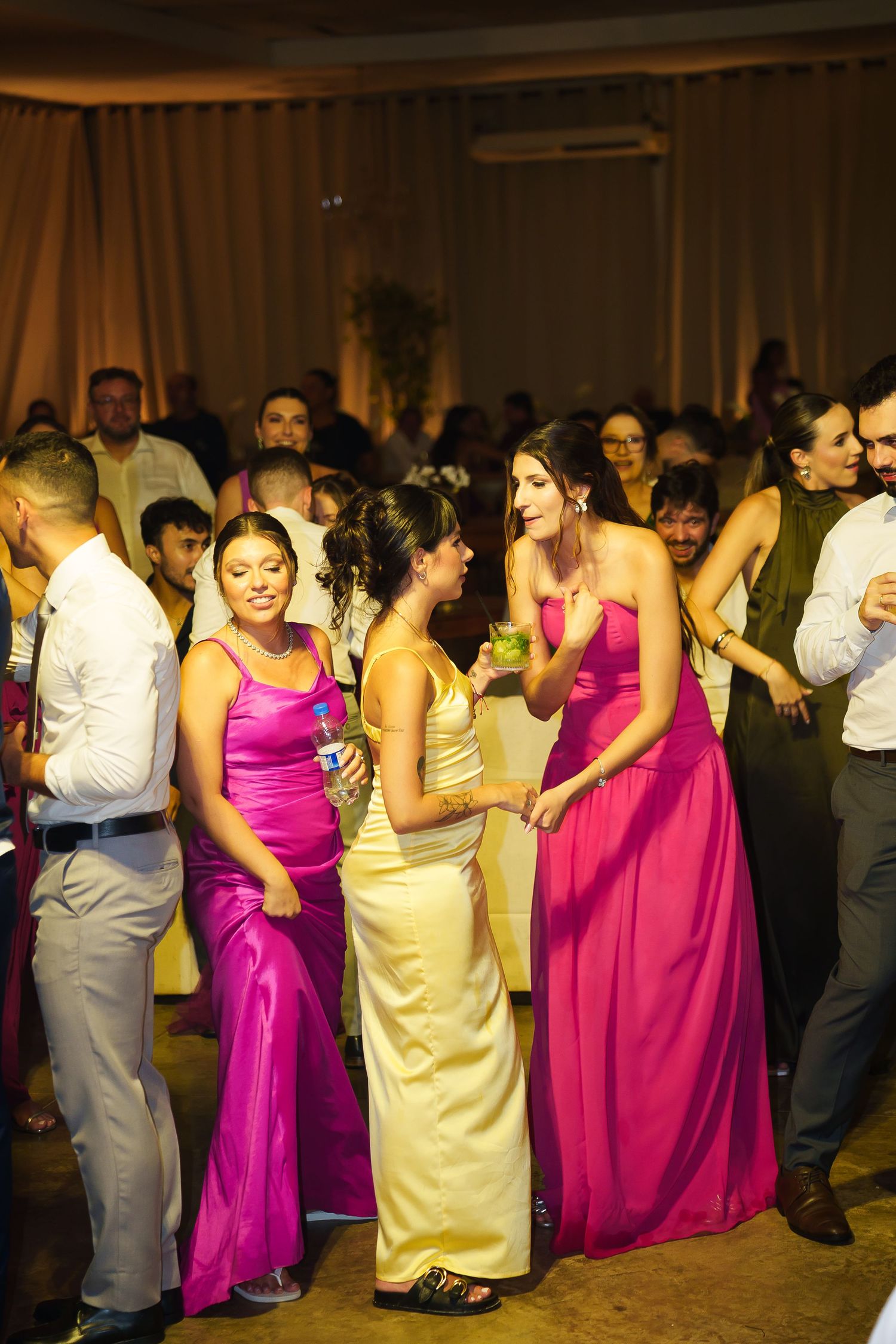 Women in colorful formal gowns dancing at a wedding reception party.