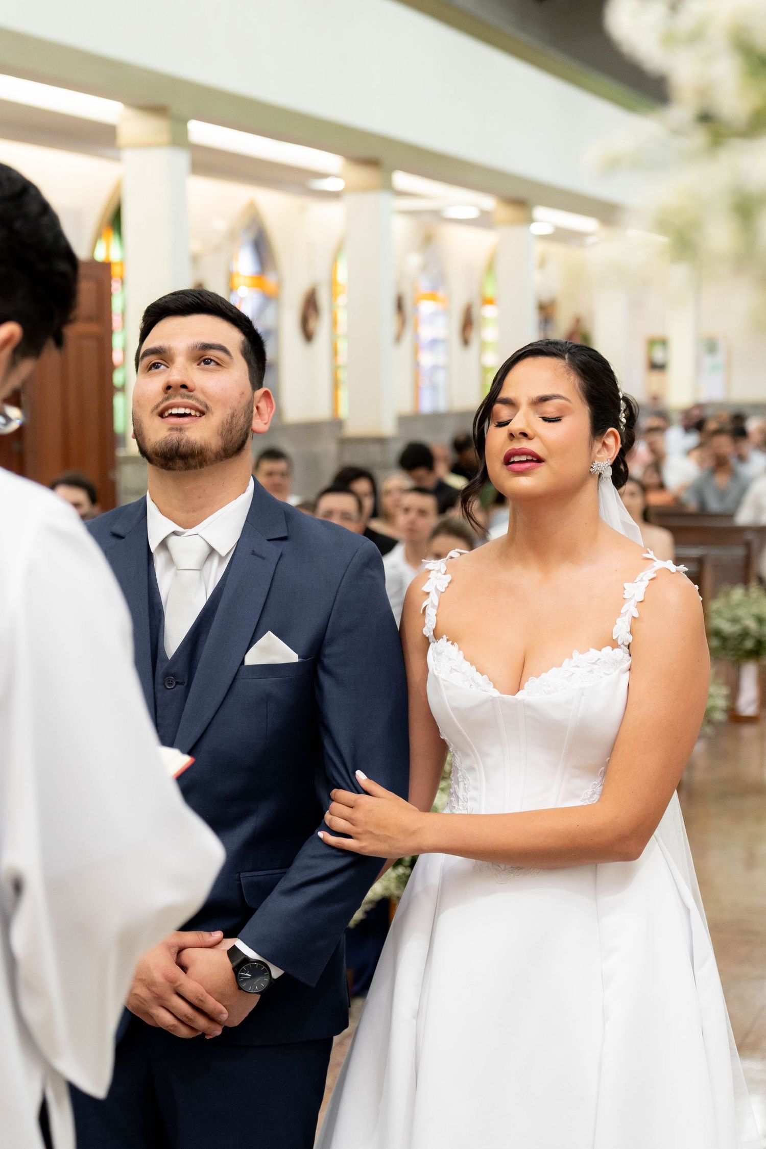 Bride and groom stand at the altar during a church wedding ceremony, bride in white gown with eyes closed.