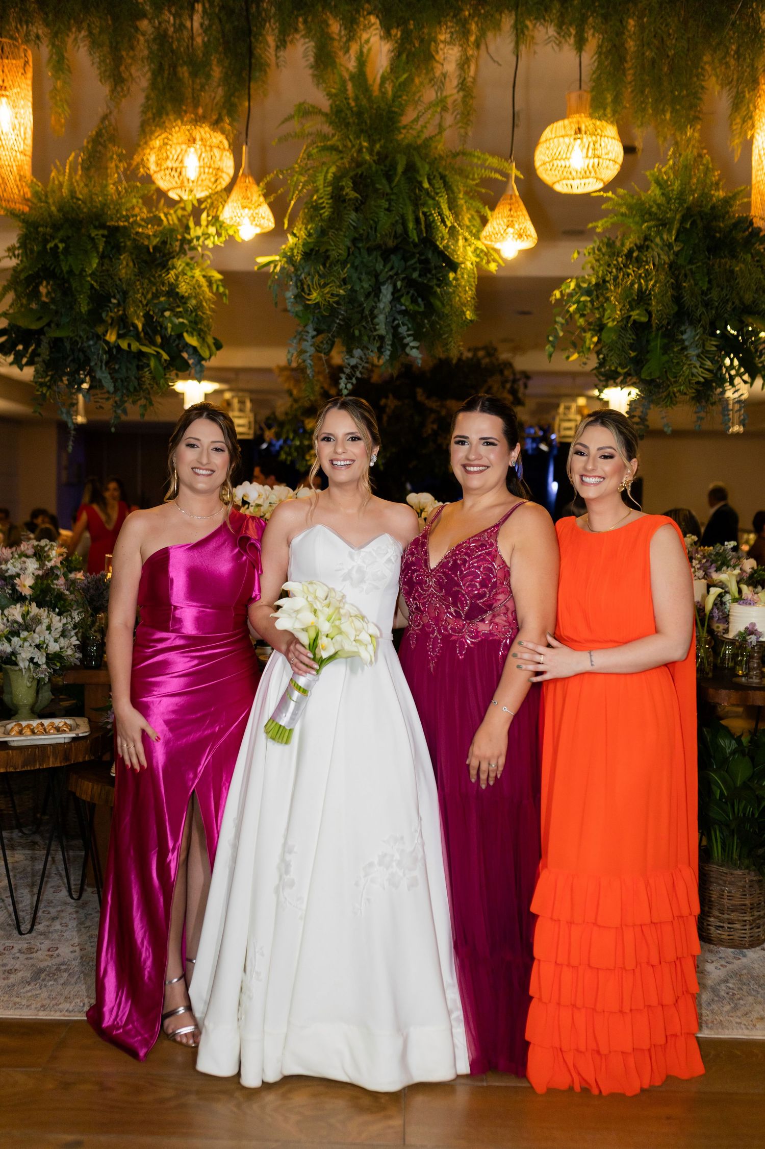 Bride in white gown poses with three bridesmaids in vibrant pink and orange dresses at an elegant wedding reception.