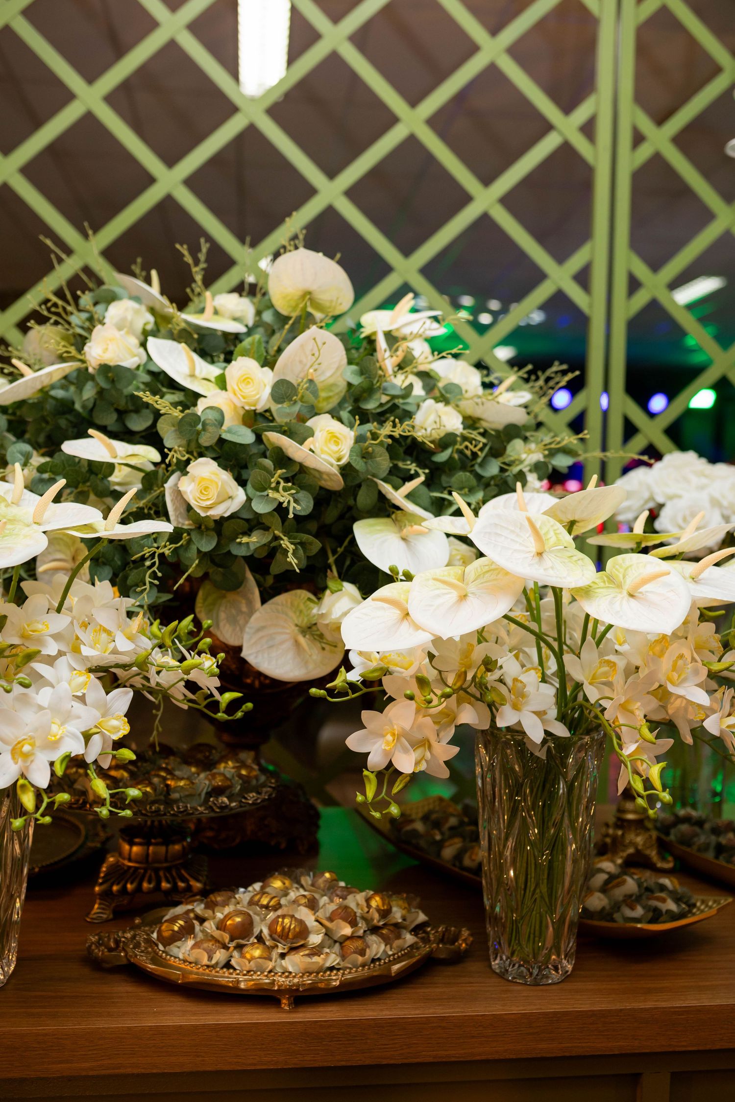 Elegant white anthurium and orchid floral arrangements with gold decorative trays on a wooden table.